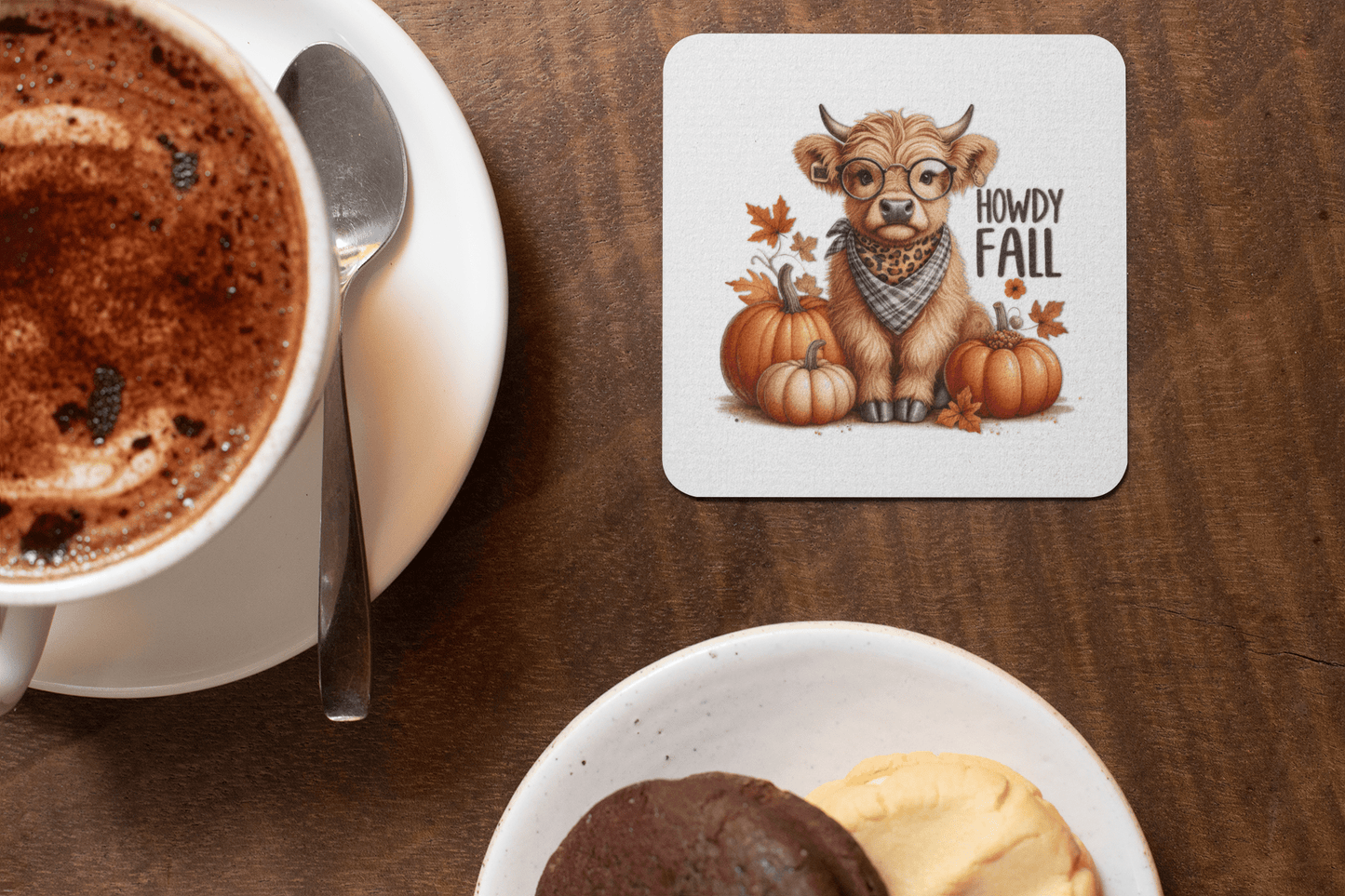 A cup of hot chocolate sits beside Mirabilia Boutique's Howdy Fall Highland Cow Coasters, featuring a cartoon cow with glasses, scarf, pumpkins, autumn leaves, and "Howdy Fall" text—perfect cute western autumn decor for a cozy fall setting. Cookies nearby.