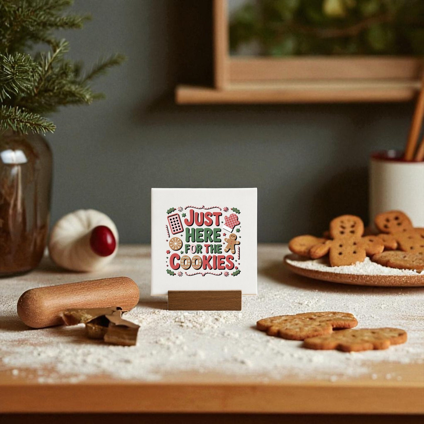 A festive kitchen displays the Mirabilia Boutique "Just Here for the Cookies" Mini Sign, surrounded by gingerbread cookies, flour, a rolling pin, and charming Christmas cookie décor—perfect cute Christmas shelf decor.