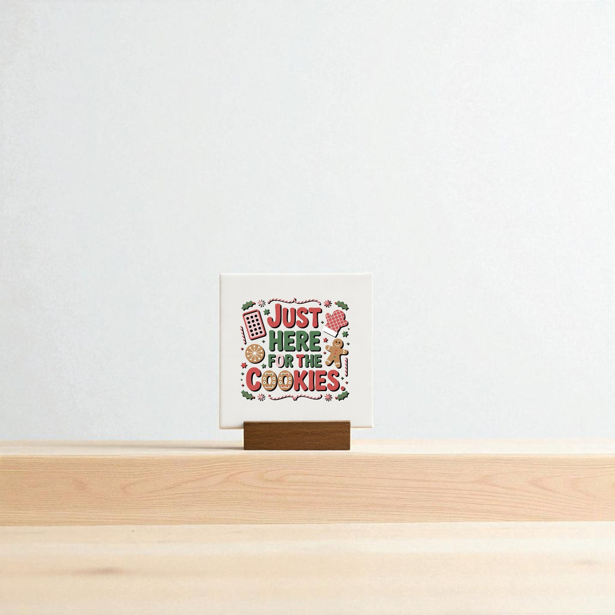 The "Just Here for the Cookies Mini Sign" by Mirabilia Boutique features playful lettering and baking illustrations on a wooden stand, making it a cute Christmas shelf decor or cookie-themed gift. Set against a plain light background.