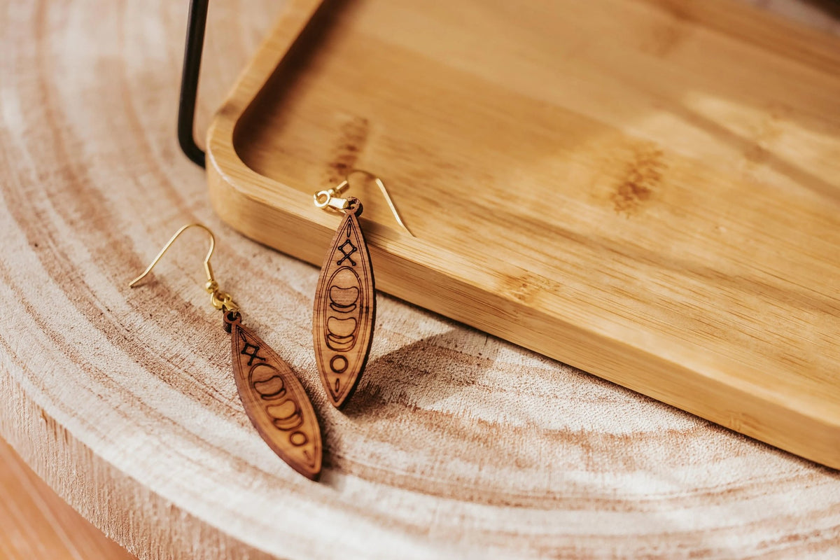 Kayak Earrings by Mirabilia Boutique—laser cut wooden dangle earrings for outdoor lovers—are displayed on a round wood surface beside a tray, creating a natural look ideal for river girls, paddlers, or canoe gift seekers.