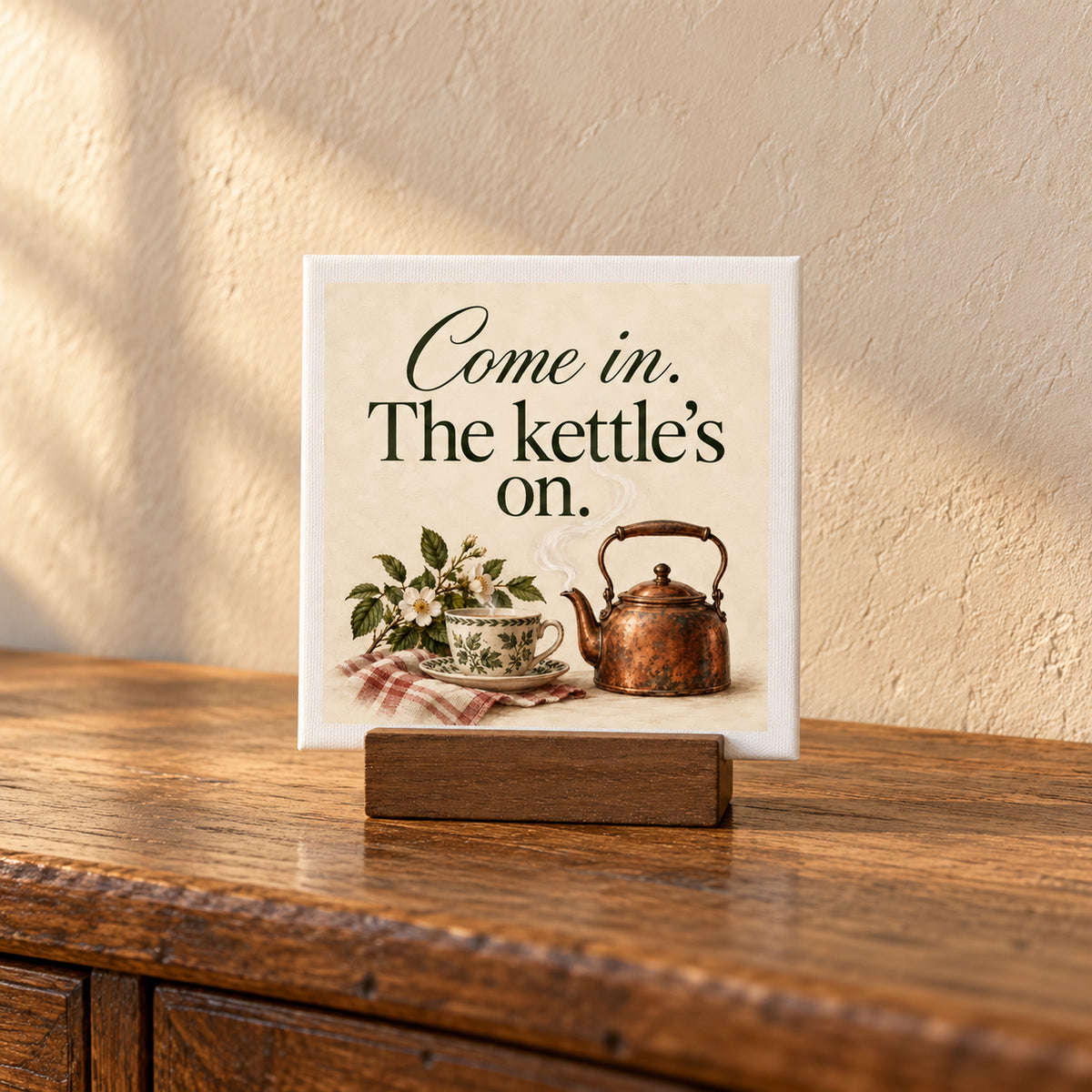 Come In, The Kettle’s On Mini Canvas on a wooden stand, featuring an illustration of a steaming copper kettle and teacup, ideal for tea corner decor.