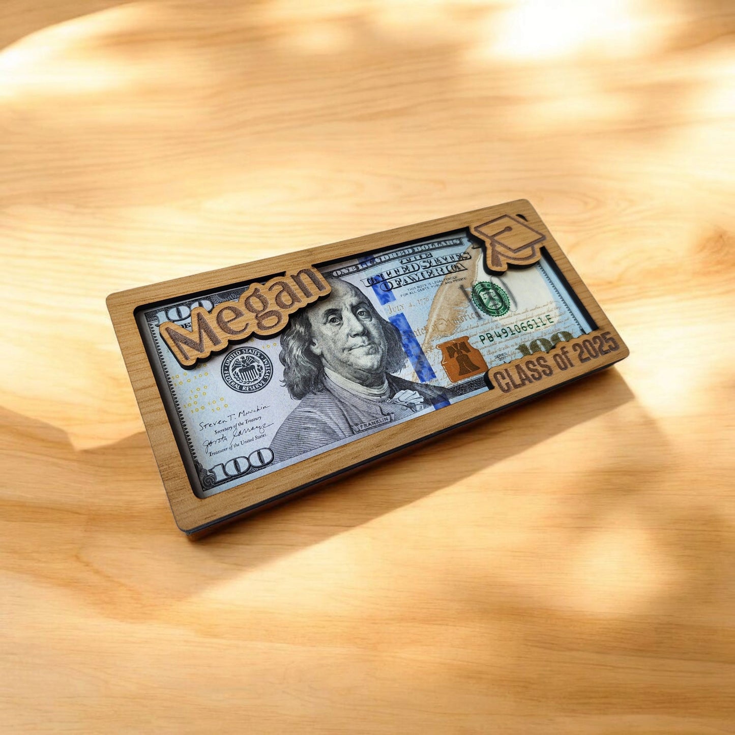 The Mirabilia Boutique Personalized Graduation Money Holder is a custom wood cash gift for the Class of 2025, featuring the graduate's name and cap design—an ideal graduation keepsake presented on light wood under sunlit shadows.