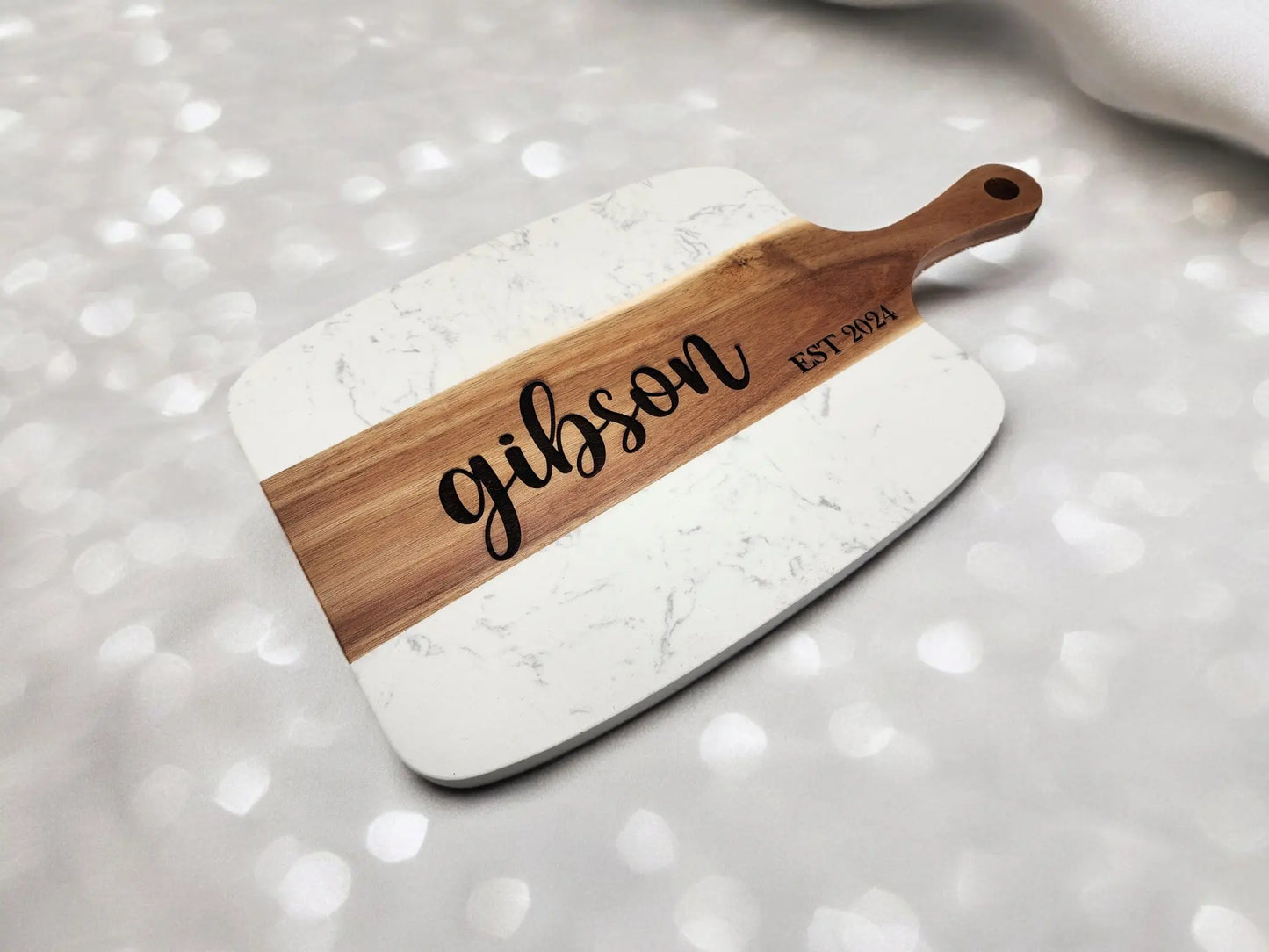 The Mirabilia Boutique Personalized Marble and Acacia Serving Board features your custom name and date engraved on the wood, making it a stylish charcuterie centerpiece or a thoughtful wedding or housewarming gift.