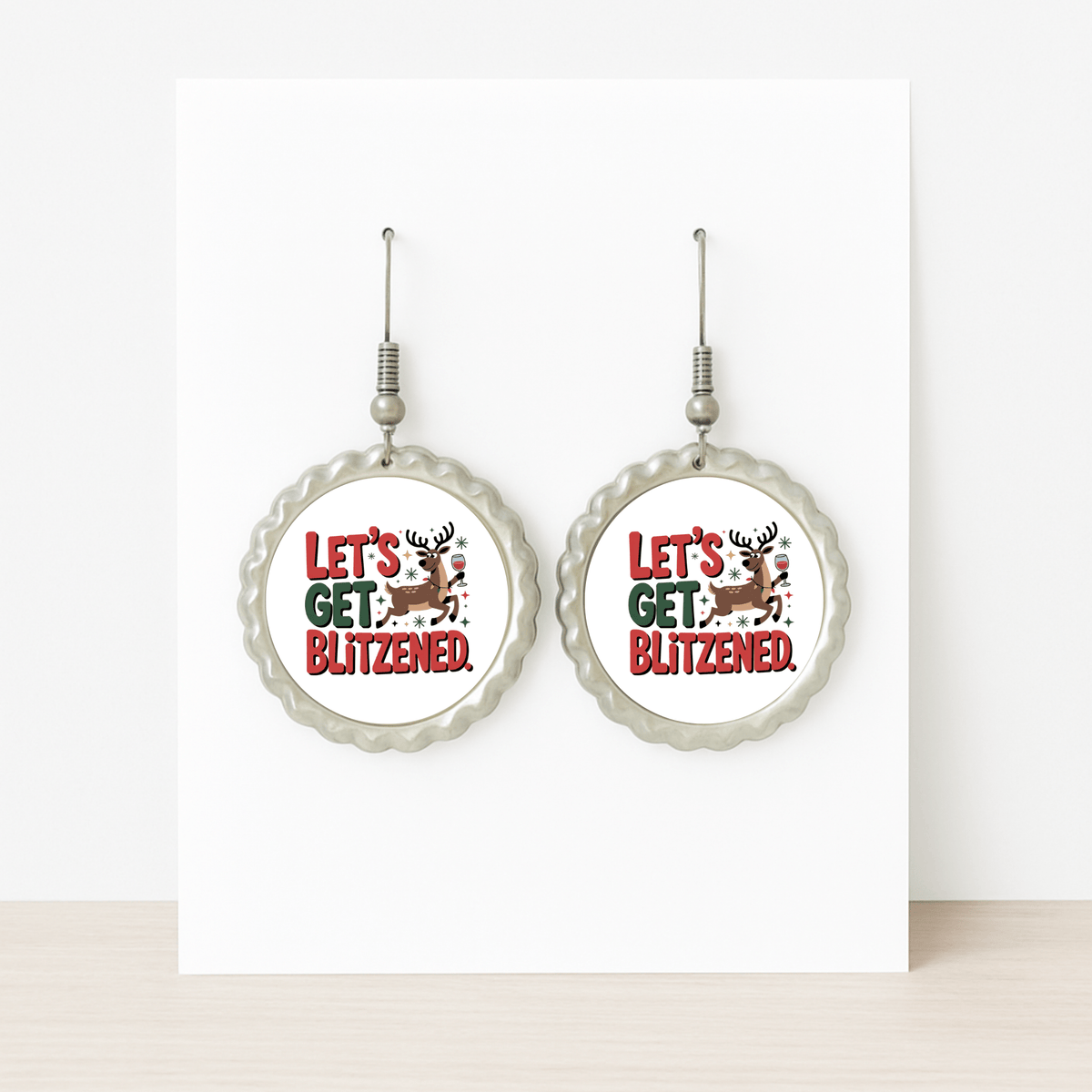 Mirabilia Boutique's "Let's Get Blitzened" round silver earrings feature a holiday reindeer and festive red & green text—funny Christmas earrings displayed on a white card, perfect for your next holiday party.
