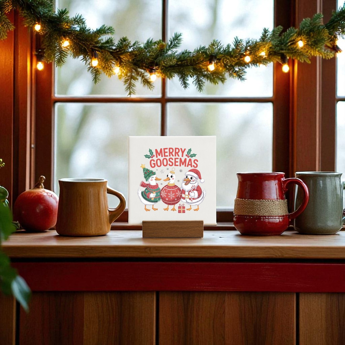 The Merry Goosemas Mini Sign by Mirabilia Boutique, featuring cartoon geese in sweaters, adds quirky holiday decor to a shelf with mugs, a pomegranate, and garland under festive string lights.