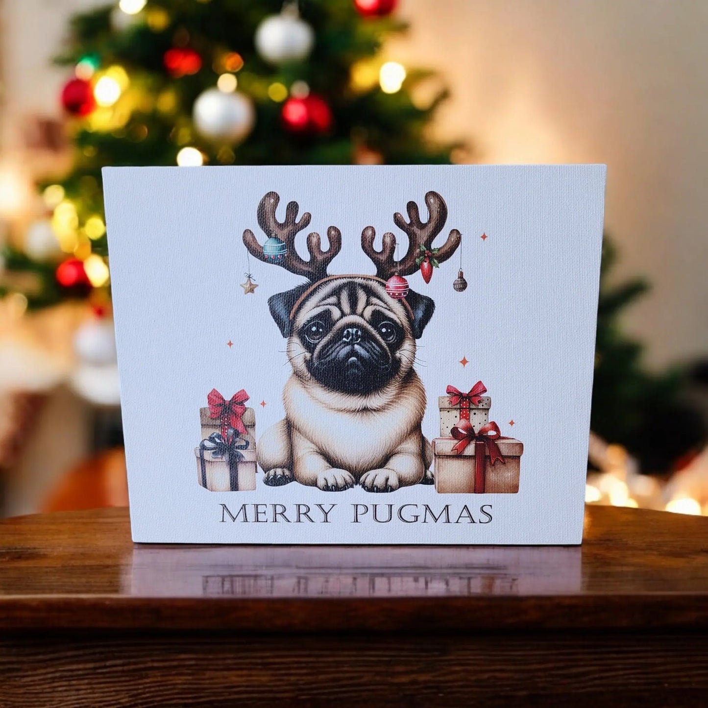 Introducing the "Merry Pugmas 10x8 Canvas Sign" by Mirabilia Boutique, a festive piece featuring an adorable pug donning reindeer antlers surrounded by wrapped gifts. The sign displays a cheerful "Merry Pugmas" message at the bottom. A beautifully decorated Christmas tree with lights and ornaments appears blurred in the background, enhancing the holiday atmosphere of this delightful scene.