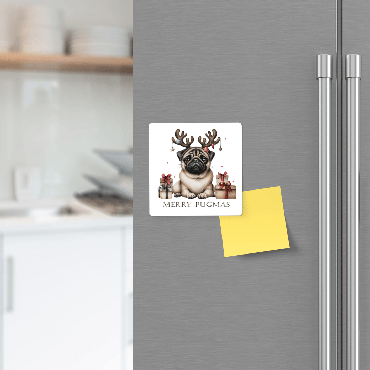 The Merry Pugmas Magnet by Mirabilia Boutique features a pug in reindeer antlers with gifts and "Merry Pugmas" text, shown on a fridge with a yellow note, kitchen counter, and festive holiday decor in the background.
