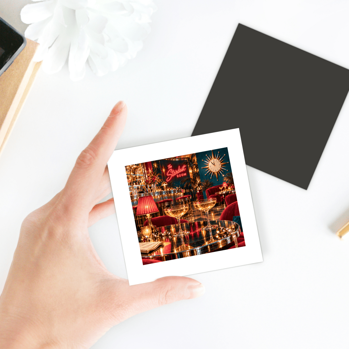 A hand holds a Five Minutes to Midnight Magnet | Chrome & Starlight, a square lounge magnet featuring a vintage scene with drinks on a table, a starburst clock, and a neon sign reading “The Stardust Room.”.