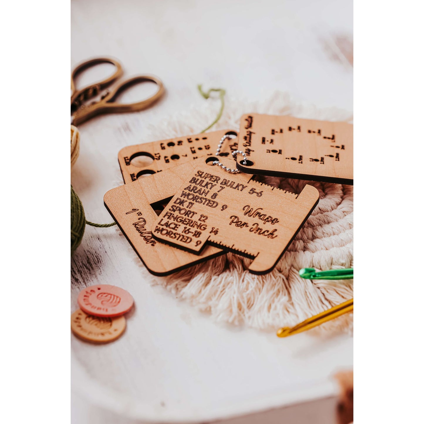 The Knitter’s Pocket Tool Set from Mirabilia Boutique, elegantly showcased on a white surface, features wooden keychains with yarn size details. It includes scissors and crochet hooks, making it perfect for travel knitting accessories or as a gift in project bags.
