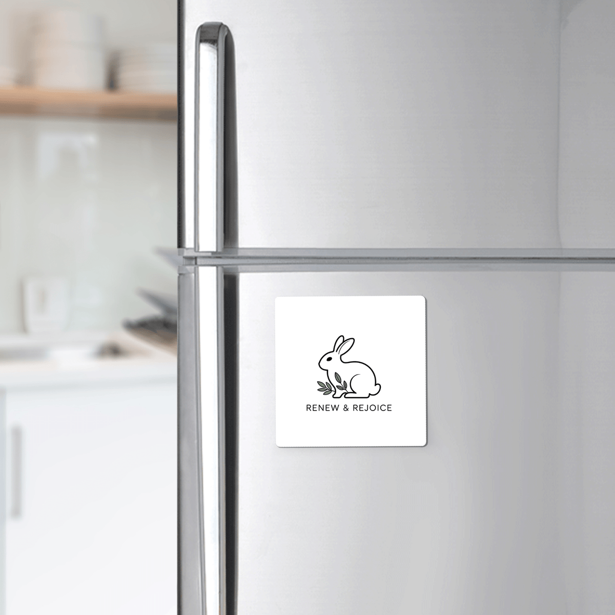 The Renew & Rejoice Magnet – Minimalist Bunny Design by Mirabilia Boutique, ideal for Easter basket fillers or mindfulness reminders, is displayed on a stainless steel fridge in a modern kitchen.