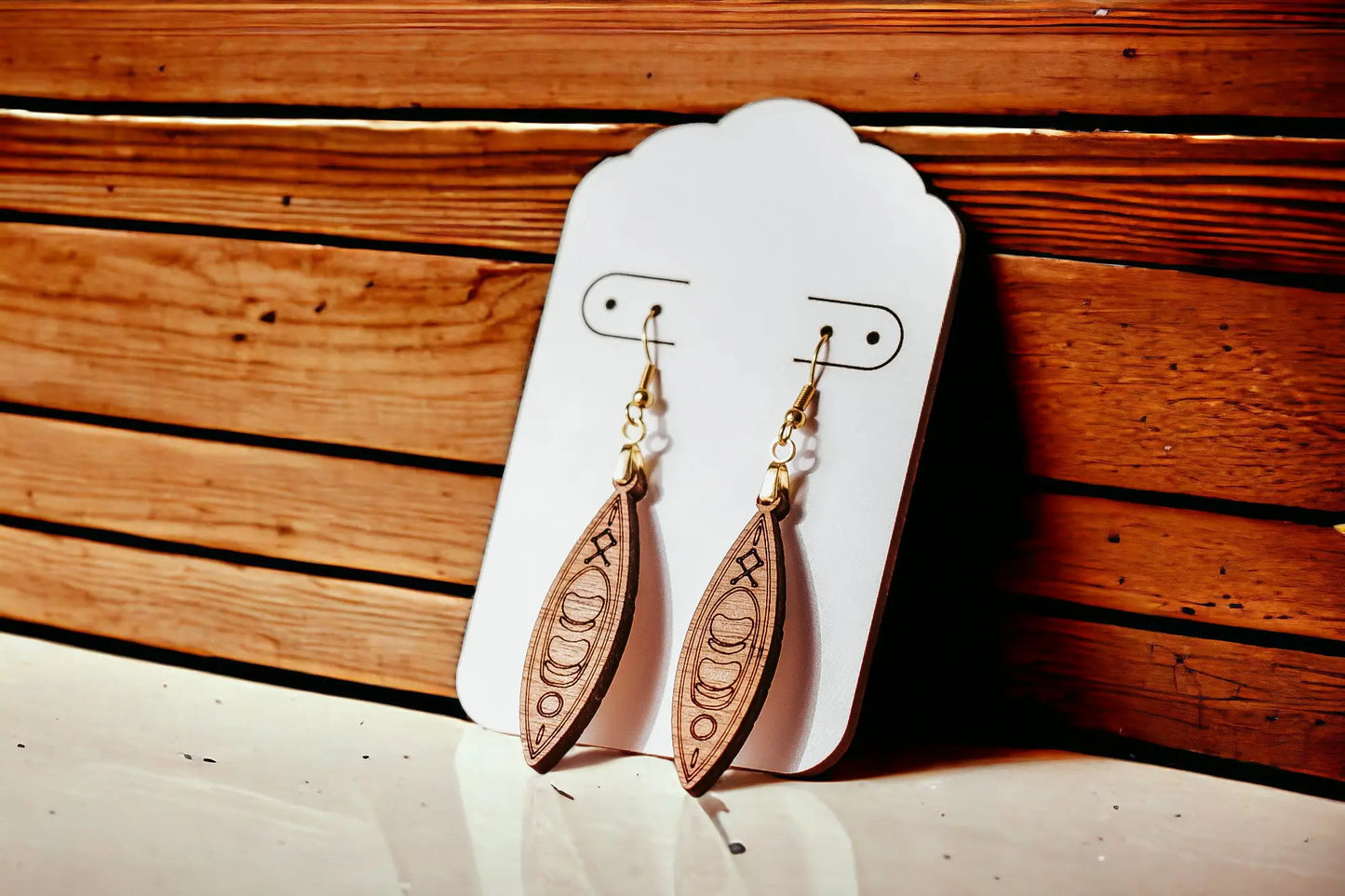 Kayak Earrings by Mirabilia Boutique—laser cut wooden dangle earrings for river girls, paddlers, and outdoor lovers—engraved and displayed on a white card against a wooden wall. Perfect canoe gift!.