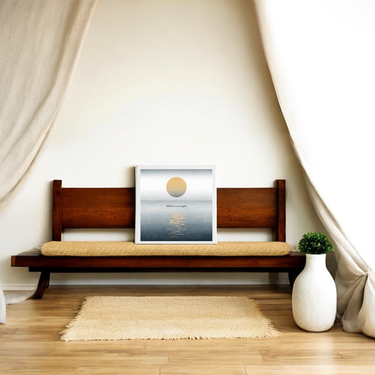 A minimalist room with a wooden bench, beige cushion, Mirabilia Boutique’s "Stillness Is Strength" Canvas Wall Art, cream curtains, woven rug, and a white vase with greenery—perfect tranquil meditation decor.