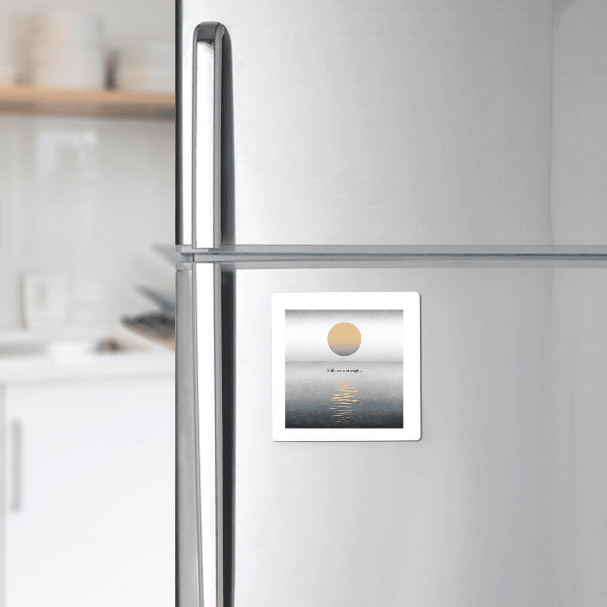 The Stillness Is Strength Magnet by Mirabilia Boutique, featuring a minimalist sun-over-water design, adds calm and warmth to your modern kitchen decor. Perfect for mindful gifting, it’s shown on a stainless steel fridge with dishes in view.