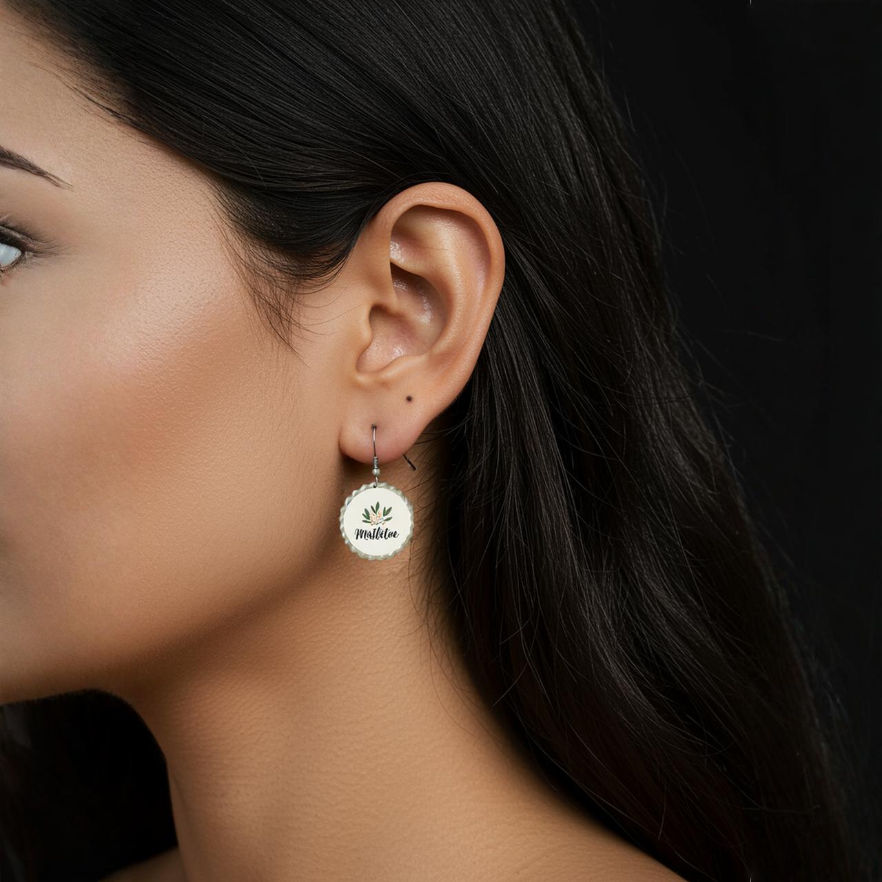 A close-up side view of a woman’s face highlights her ear adorned with Mirabilia Boutique’s Mistletoe Holiday Earrings, a pair of round, gold botanical Christmas jewelry engraved with a leaf design and “mother,” against a solid black background.
