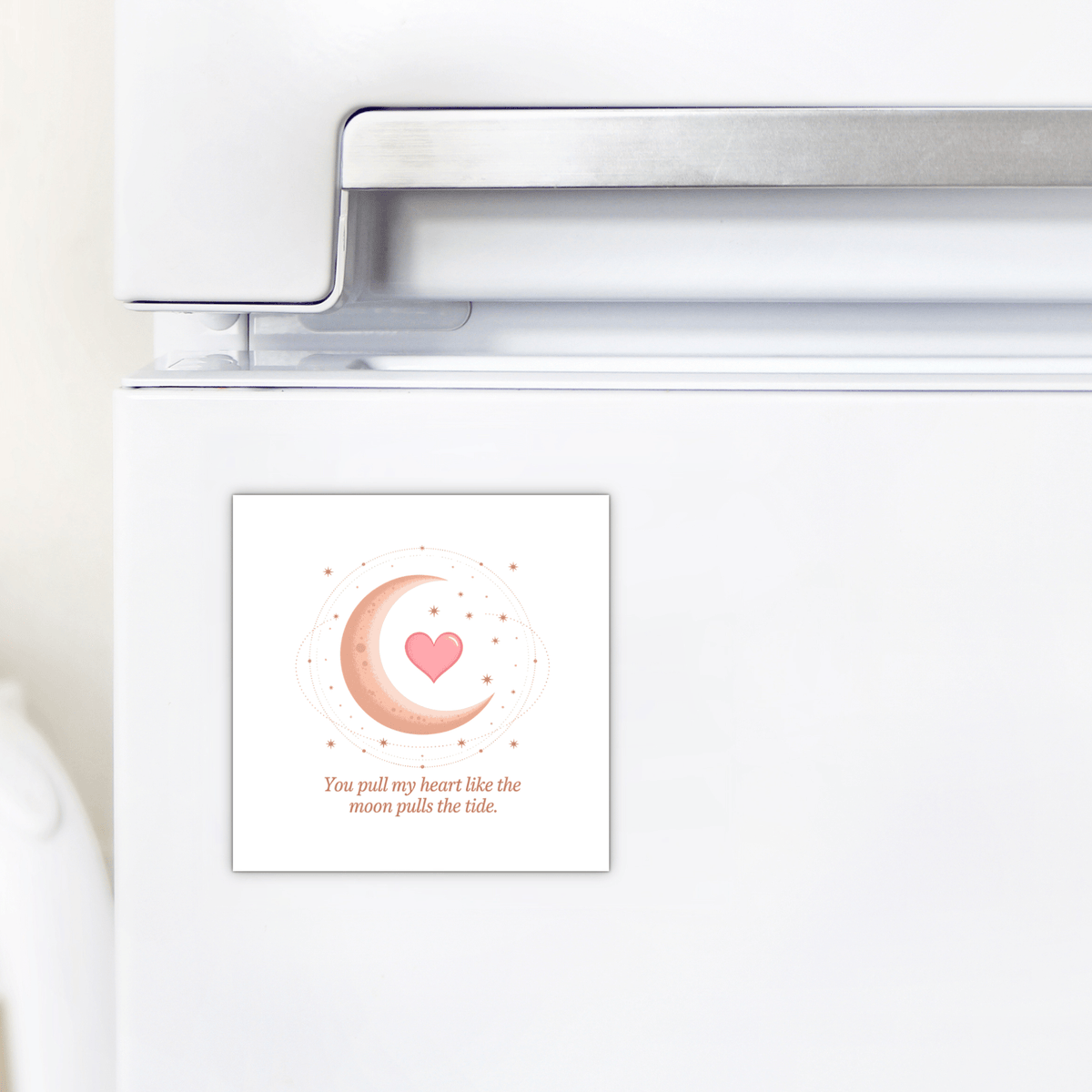 A white fridge with the Mirabilia Boutique Moon and Heart Love Quote Magnet, featuring a pink crescent moon, heart, stars, and the phrase “You pull my heart like the moon pulls the tide”—ideal as a romantic gift or moon heart decor.