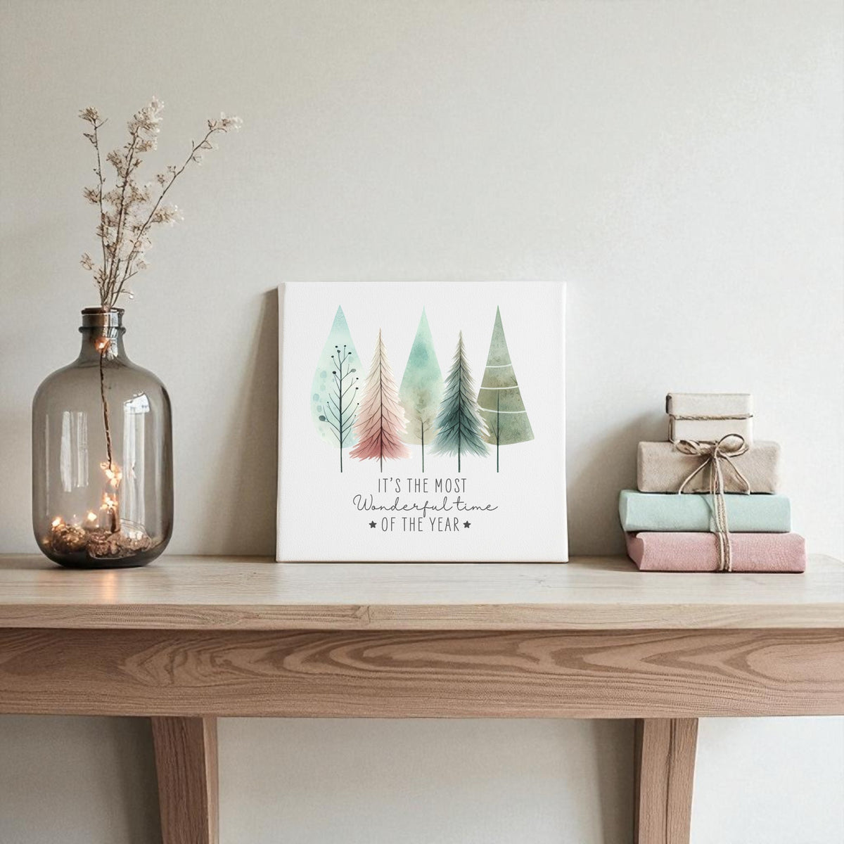 A table featuring the Most Wonderful Time of Year Canvas with pastel watercolor trees by Mirabilia Boutique and a vase of books creates charming winter decor.