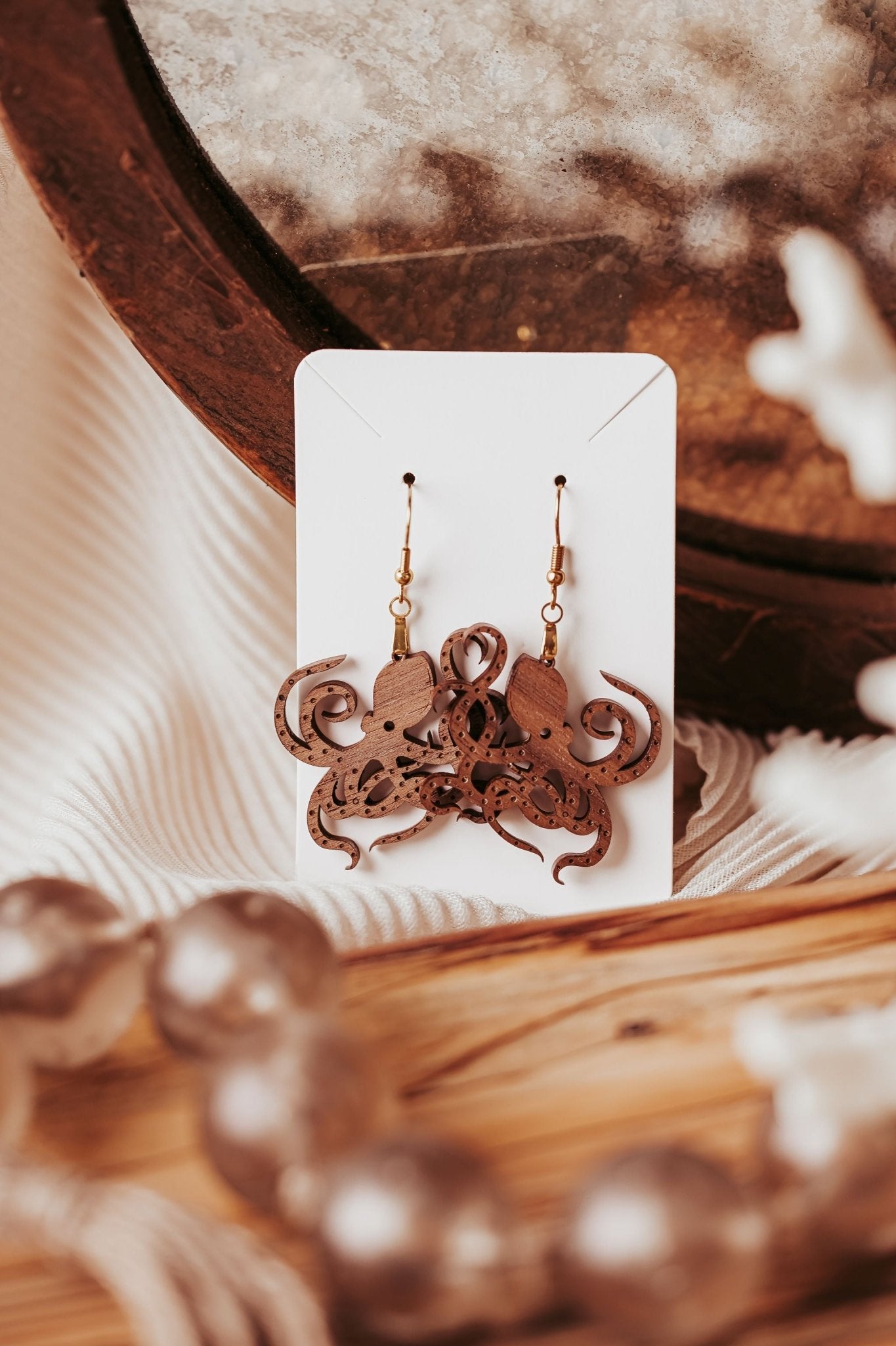 Octopus Earrings by Mirabilia Boutique—laser-cut from walnut wood, shown on a white card against a textured background with soft lighting and decorative foreground elements. Perfect ocean jewelry gift for nature or sea life lovers.