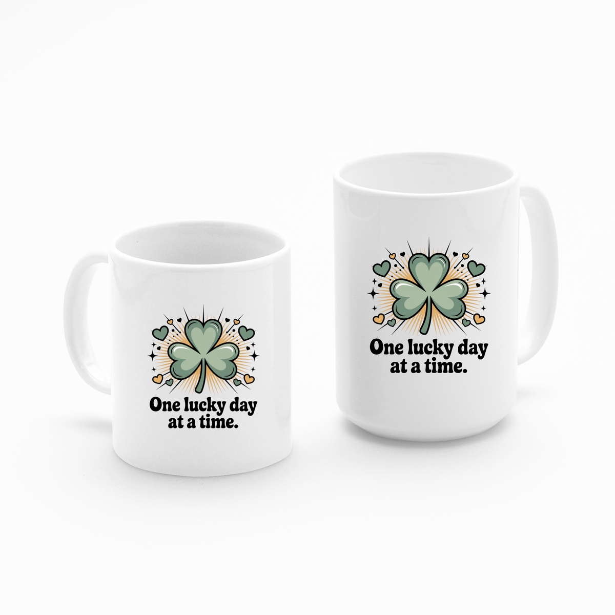 The Mirabilia Boutique "One Lucky Day at a Time Mug – Shamrock Ceramic Cup" features white ceramic, green four-leaf clovers, the uplifting phrase, and is decorated with hearts, stars, and gold coins on each mug.