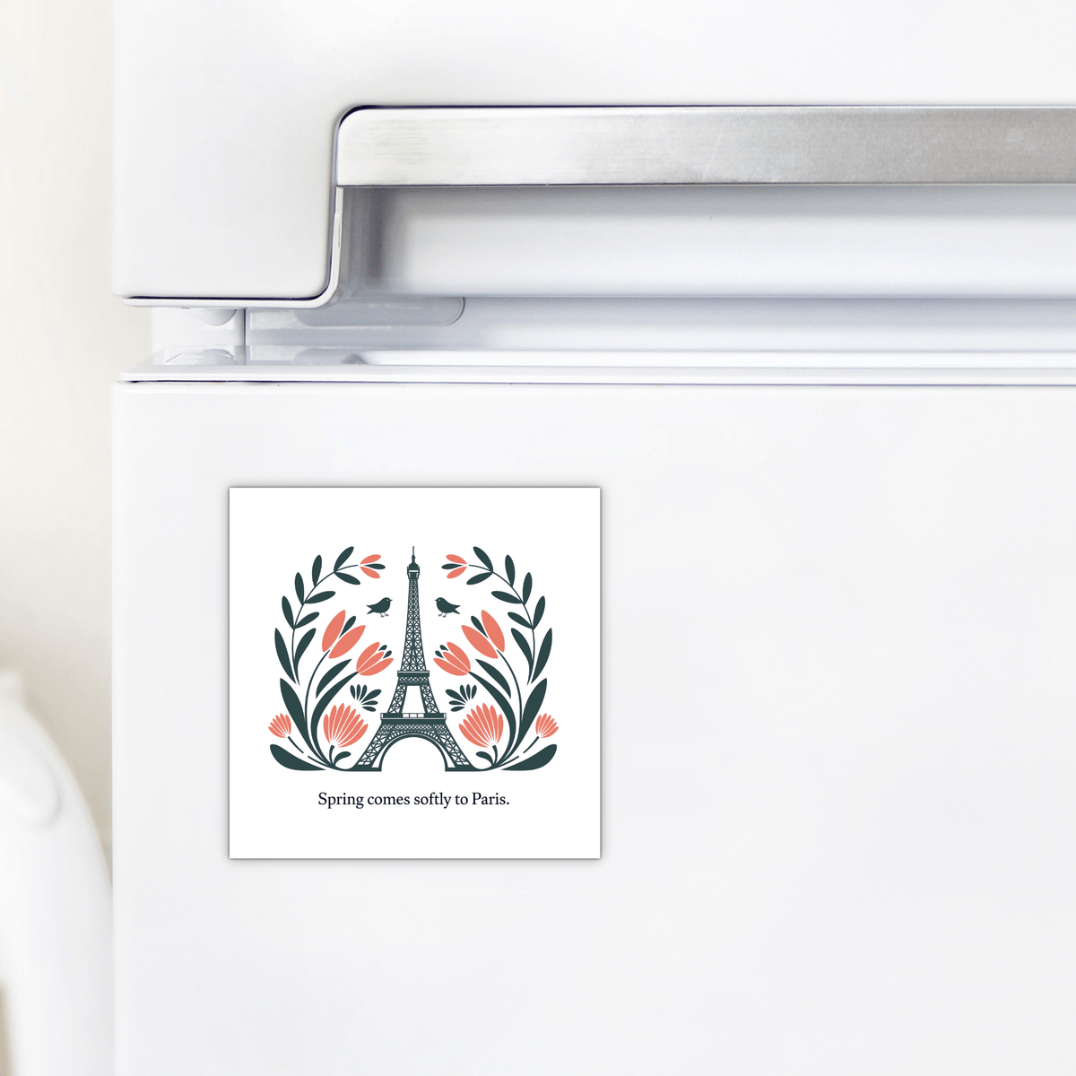 The Mirabilia Boutique Spring Comes Softly to Paris – Floral Eiffel Magnet features the Eiffel Tower with leaves and pink flowers, plus the text "Spring comes softly to Paris." Perfect for your refrigerator!.