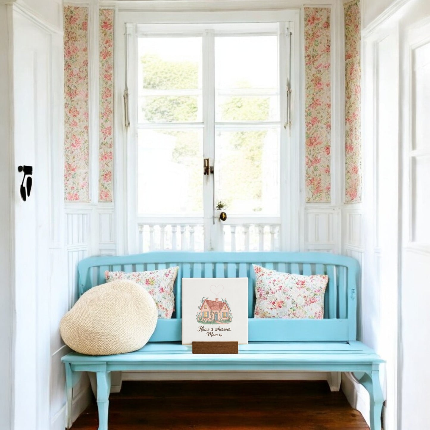 In a cozy, vintage-style room, the Mirabilia Boutique "Home Is Wherever Mom Is" Mini Sign makes a thoughtful Mother’s Day gift, pairing beautifully with light blue wooden furniture and floral cushions by a bright window.