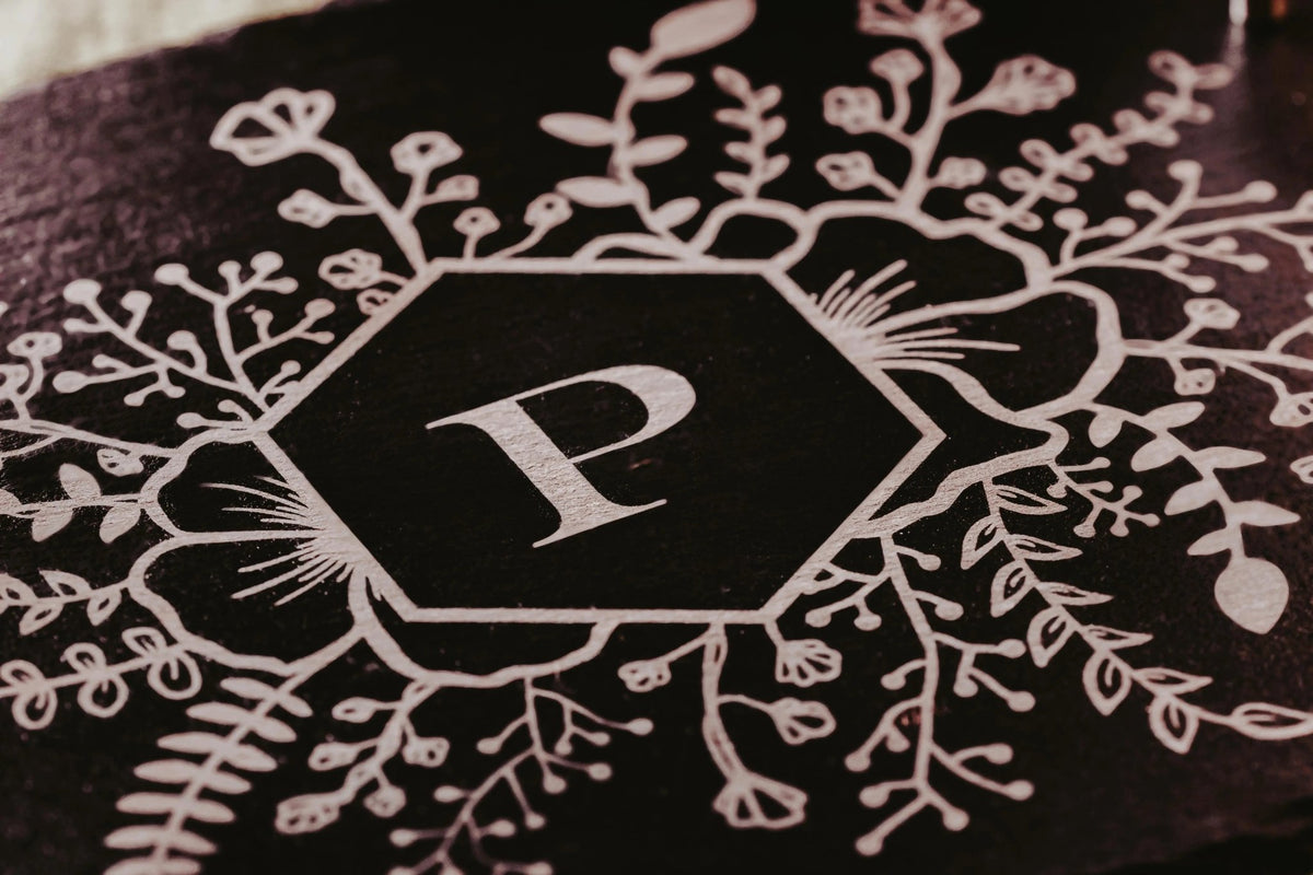 A white floral monogram encircles a black hexagon with a bold "P," set against a dark background—ideal for Mirabilia Boutique’s Personalized Engraved Slate Serving Tray with Handles, making it a unique custom gift.