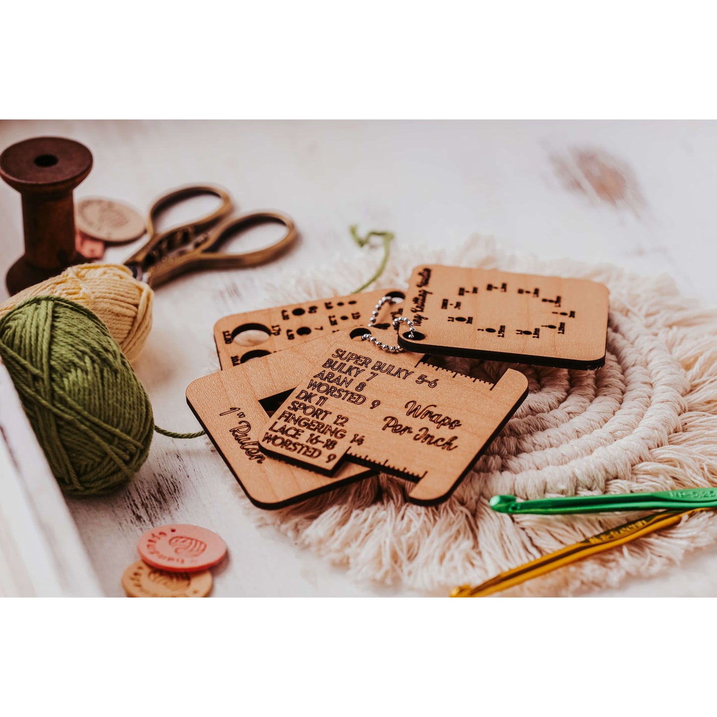 Mirabilia Boutique's Knitter’s Pocket Tool Set, featuring 4 mini tools, is beautifully arranged on a textured mat with yarn, scissors, and a spool to create a cozy crafting scene.
