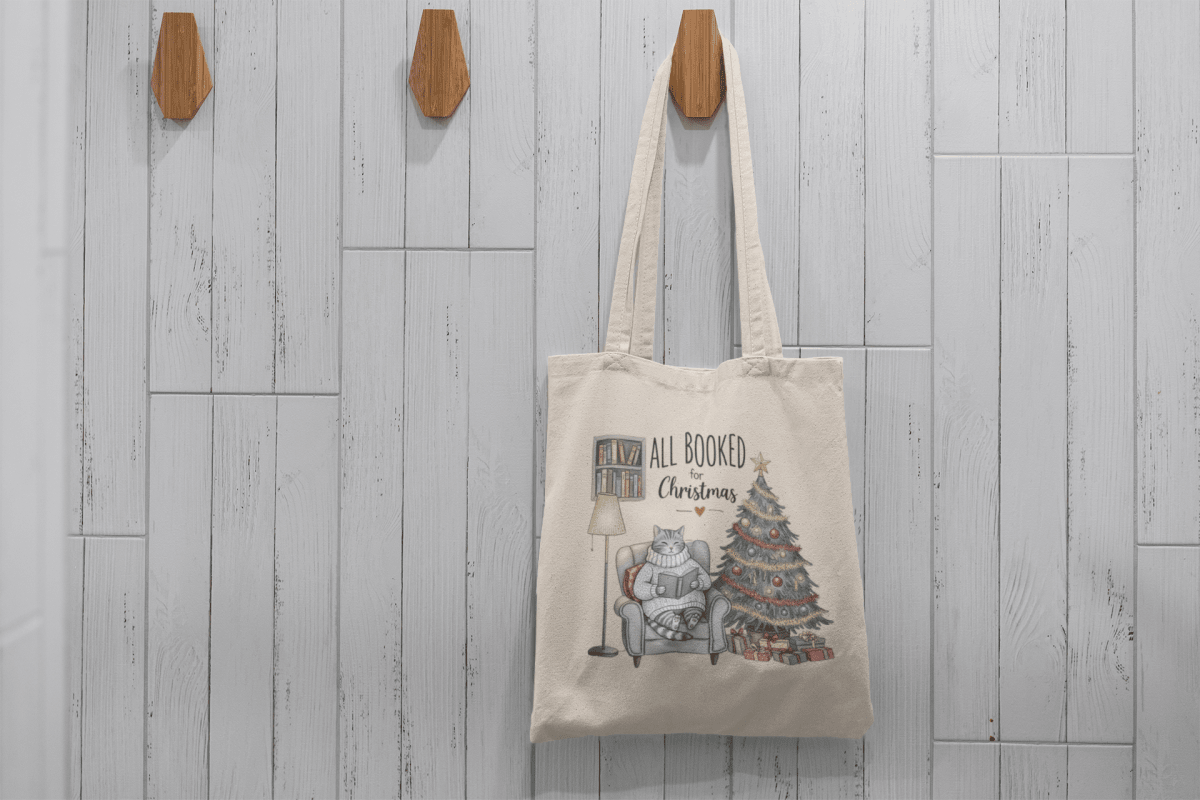 The Mirabilia Boutique “All Booked for Christmas Cat Tote Bag” is a beige tote featuring a cat reading by the tree—perfect as a cozy holiday accessory or gift for book lovers.