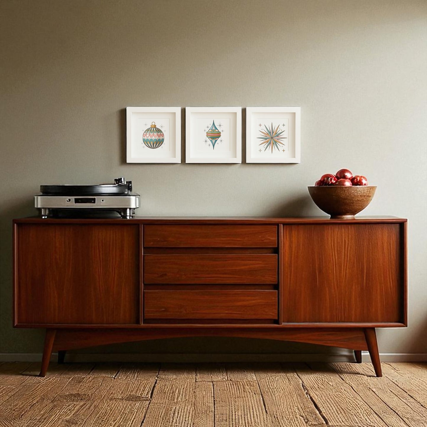 A mid-century wooden sideboard holds a record player and red apples, with the Retro Ornament Trio Holiday Wall Art Set by Mirabilia Boutique displayed above. Three geometric prints hang on the neutral wall, and a textured woven rug covers the floor.