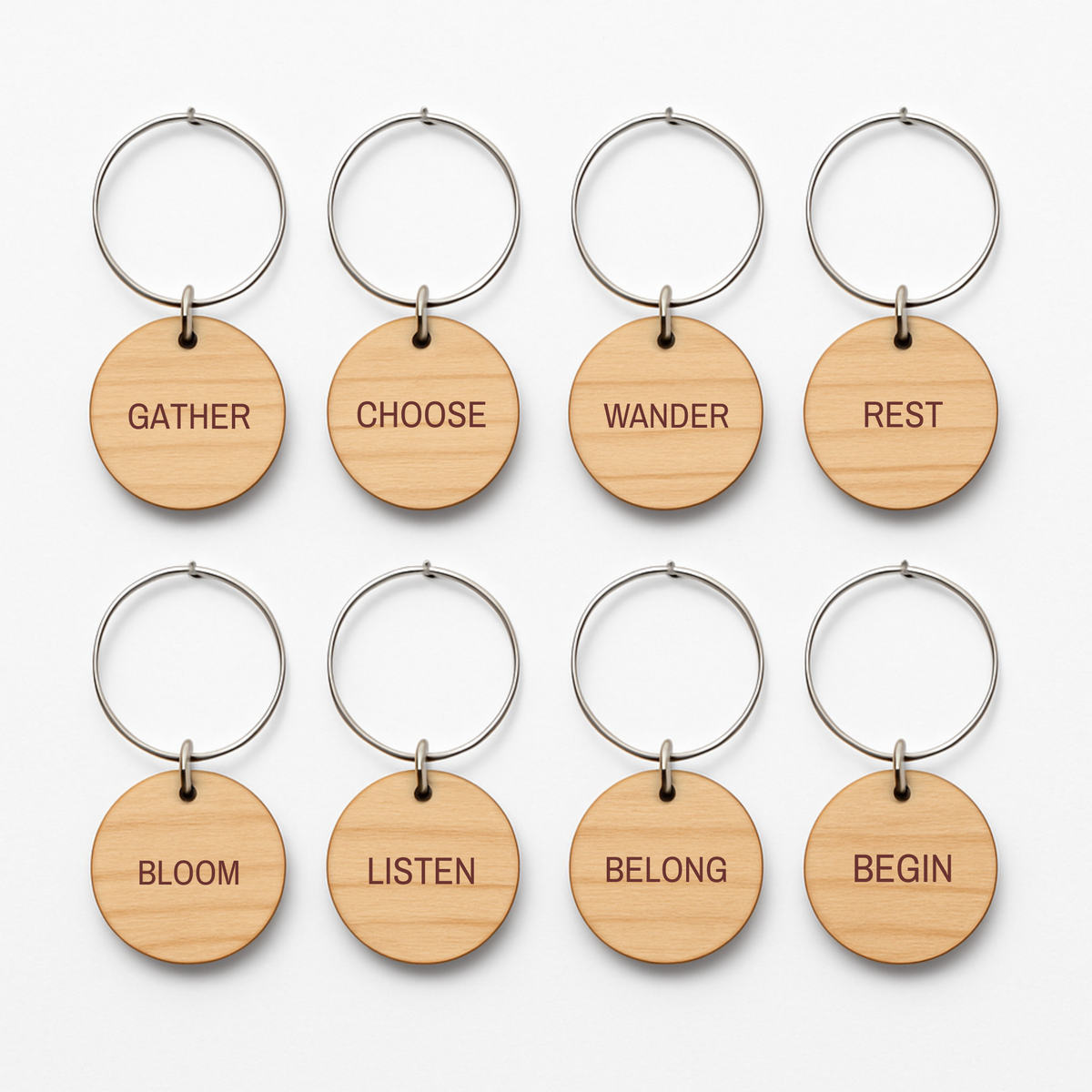 Sand & Saffron Wine Charms set of 8: eight circular wooden wine charms, each hanging from a silver hoop and engraved with a different word: Gather, Choose, Wander, Rest, Bloom, Listen, Belong, and Begin.