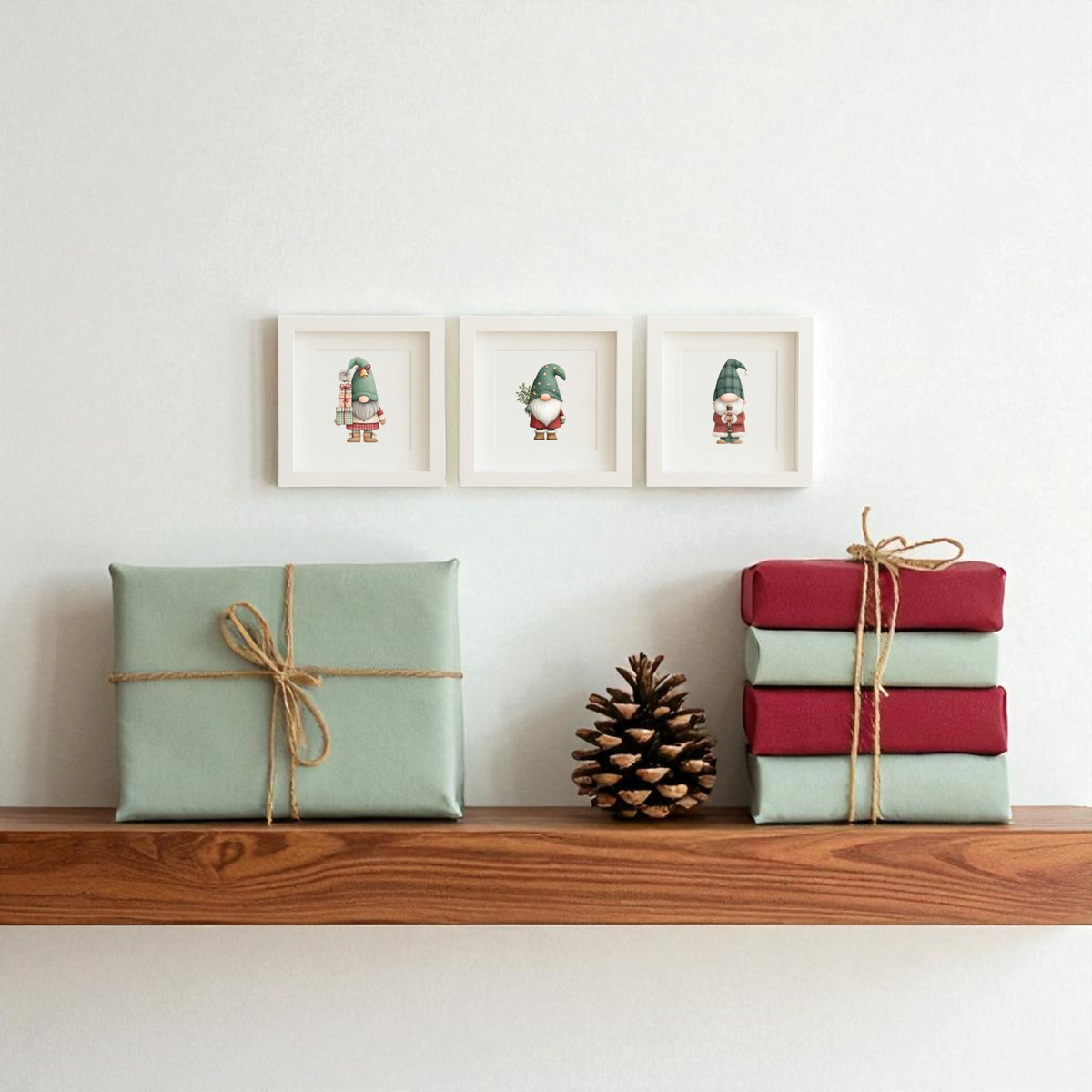 A wooden shelf with three wrapped gifts and a pine cone sits below the Scandinavian Gnome Art Trio | Framed Christmas Decor by Mirabilia Boutique, adding playful holiday charm to the white wall.