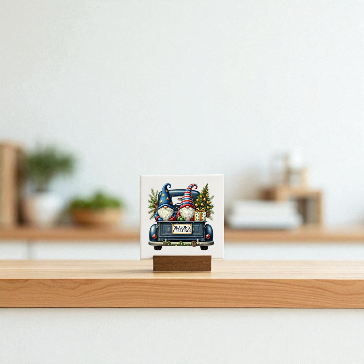 The Mirabilia Boutique Season’s Greetings Gnome Mini Sign, a 4x4 holiday canvas featuring a festive gnome scene and “Merry Christmas” message, sits on a wooden stand atop a light surface with a softly blurred background.