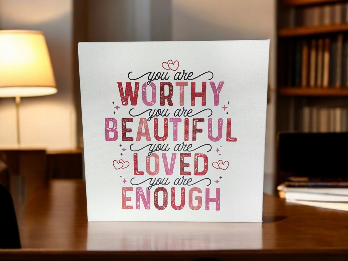 The Mirabilia Boutique "You Are Worthy Affirmation Sign" is an 8x8 inch inspirational canvas wall art for women or teens, featuring pink and red text with hearts—perfect self-love decor or a positive affirmation gift. Lamp and bookshelf shown in the background.