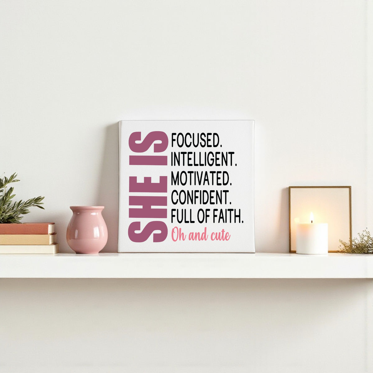 On a white shelf, the Mirabilia Boutique “She Is Focused Motivated Confident” 8x8 canvas inspires with bold affirmations. A pink vase, white candle, and small plant complete this perfect motivational wall art.