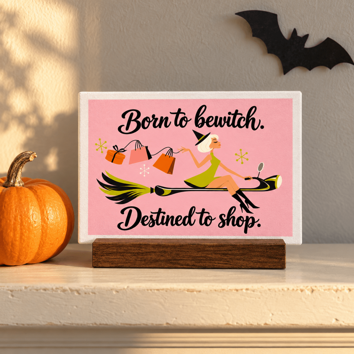 A Little Retail Magic Mini Sign on a wooden base featuring a cartoon witch flying on a broomstick with shopping bags and the caption “Born to bewitch. Destined to shop,” in a retro Halloween style.