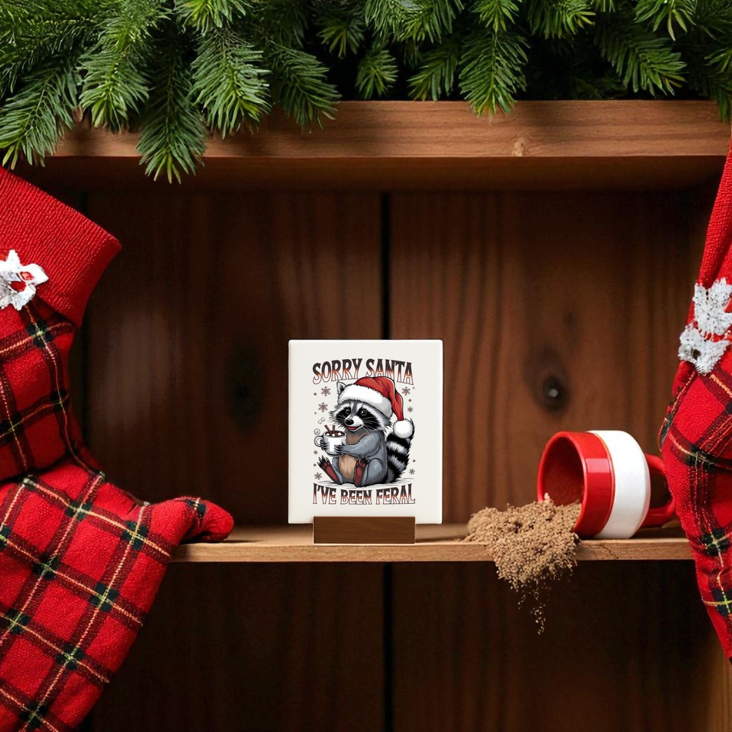 A festive shelf with red plaid stockings, a spilled jar of brown sugar, pine branches, and the “Sorry Santa I’ve Been Feral” Sign by Mirabilia Boutique—featuring a funny raccoon in a Santa hat—creates the perfect holiday look.