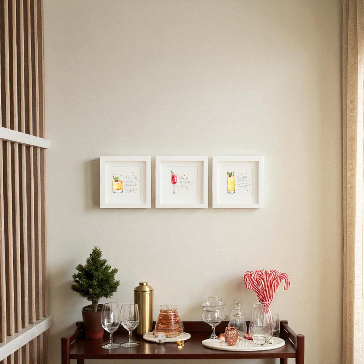 A small bar cart with glasses, a shaker, candy canes, and a mini tree sits beneath Mirabilia Boutique's "Sparkly Holiday Cocktails" 5x5 Shadowbox Trio festive bar art on a beige wall in a cozy, well-lit room.