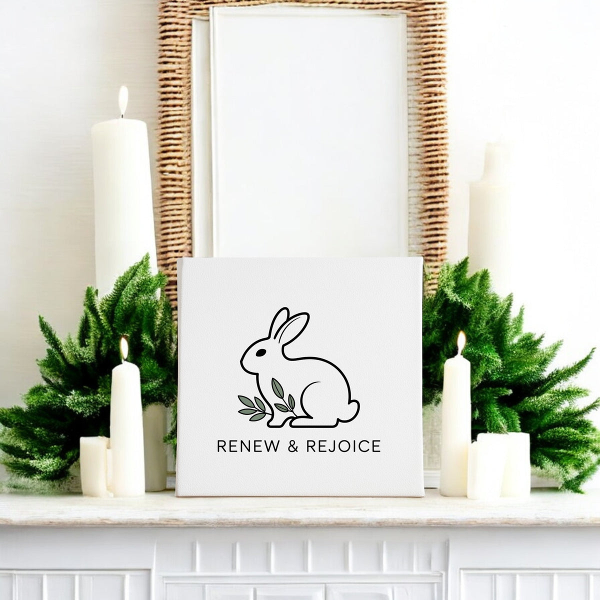 A white mantel with green foliage and white candles displays the Mirabilia Boutique Renew & Rejoice Bunny Canvas – 8x8 Spring Wall Art, featuring “RENEW & REJOICE.” A woven mirror above completes this charming Easter decor.