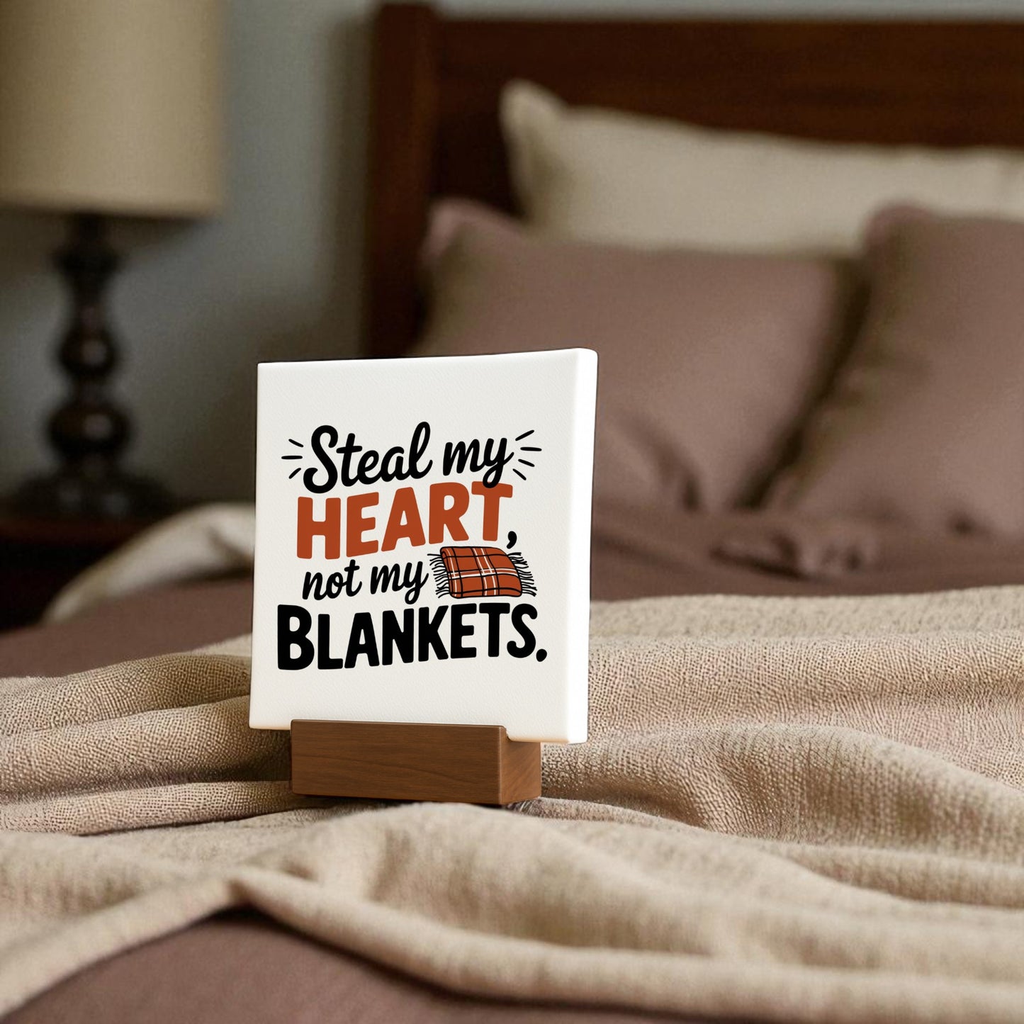 The Steal My Heart Mini Sign by Mirabilia Boutique sits on a bed with beige sheets and pillows. Featuring the quote “Steal my heart, not my blankets” and a blanket illustration, it’s perfect romantic decor or a cute couple gift.