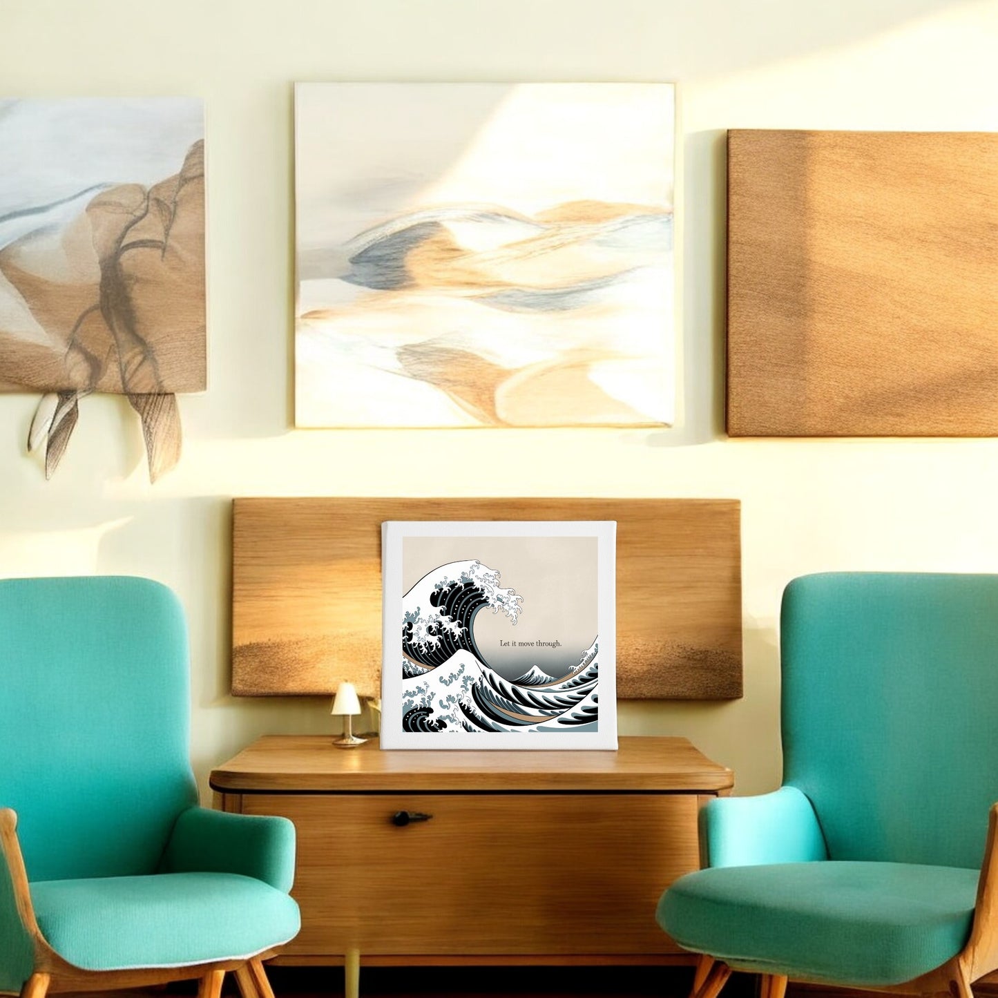 Two teal chairs face a small wooden table topped with the Let It Move Through Canvas – Bold Ocean Calm Art by Mirabilia Boutique, set against a wall with abstract paintings in neutral tones. Sunlight fills this cozy, modern room with calm and resilience.