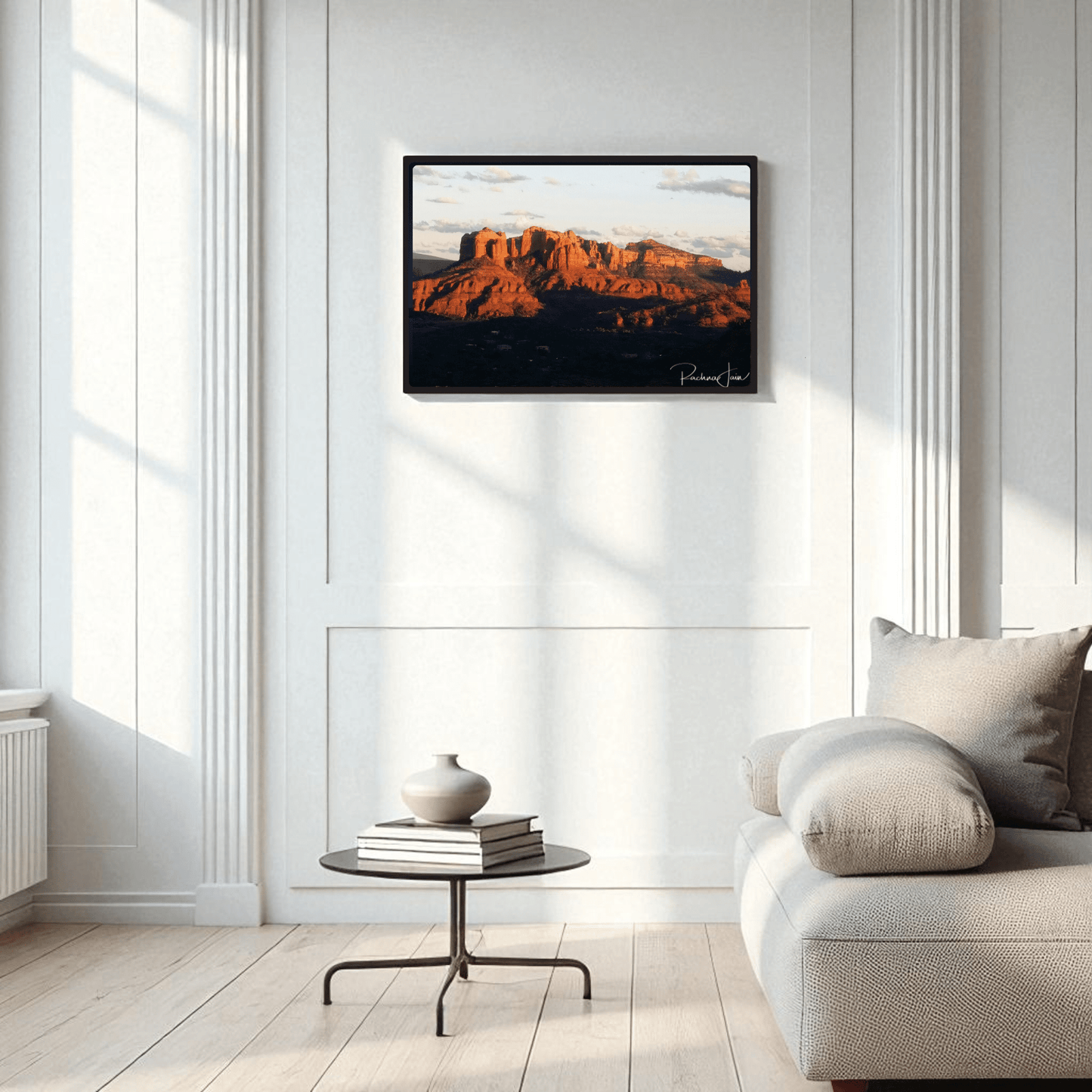 The Sunset in Sedona framed art print by Rachna Jain from Mirabilia Boutique hangs above a modern round table with vases, beside a light sofa in an elegant, bright living room with tall panels and large windows.
