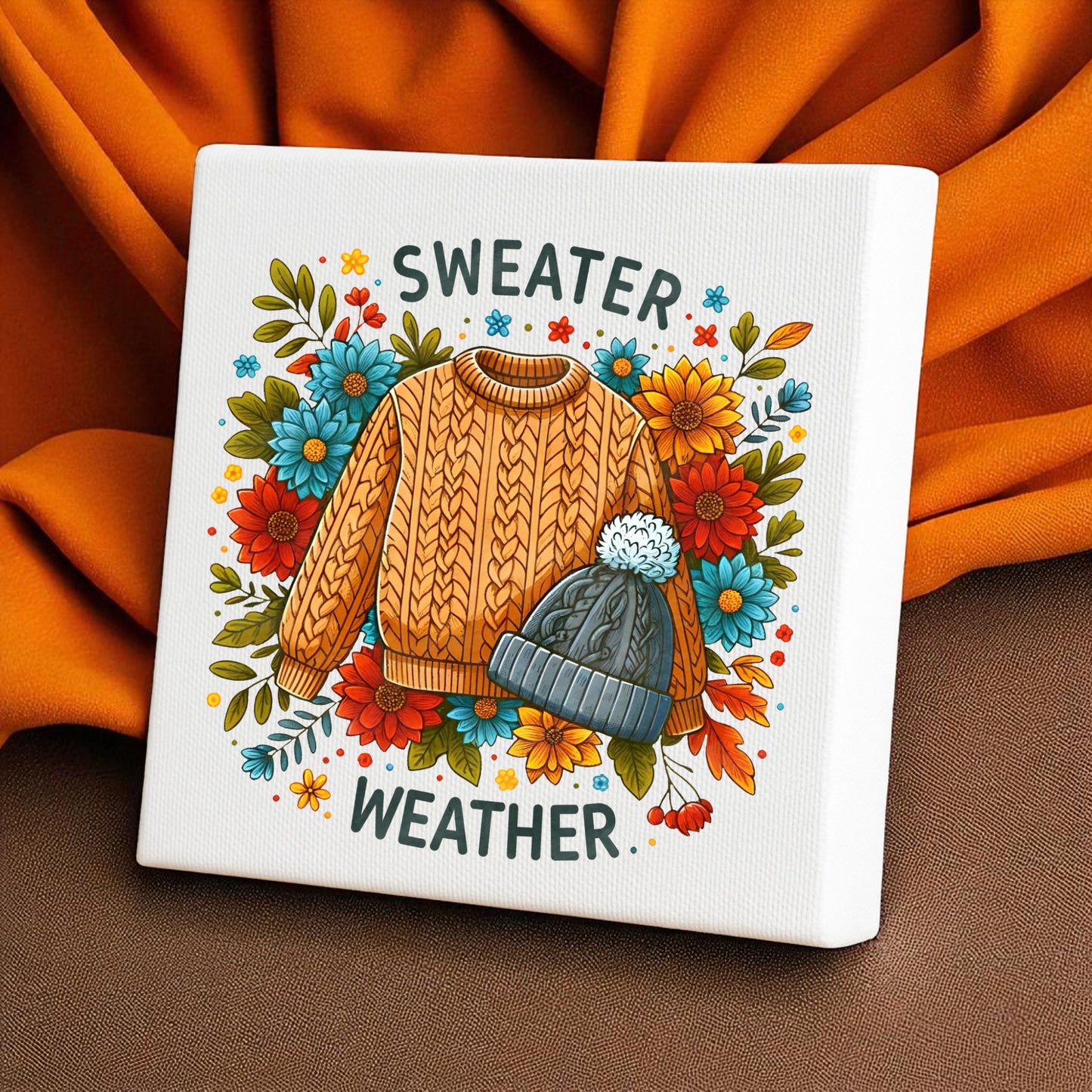 Add fall charm to your space with the Mirabilia Boutique Sweater Weather Canvas (8x8). This wall art features a knit sweater and beanie among autumn flowers on a warm orange background—perfect cozy decor for your home.