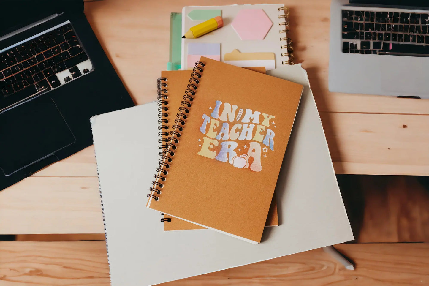 The In My Teacher Era Notebook by Mirabilia Boutique, an aesthetic spiral journal, sits among stationery on a desk—making it the perfect back-to-school teacher gift.