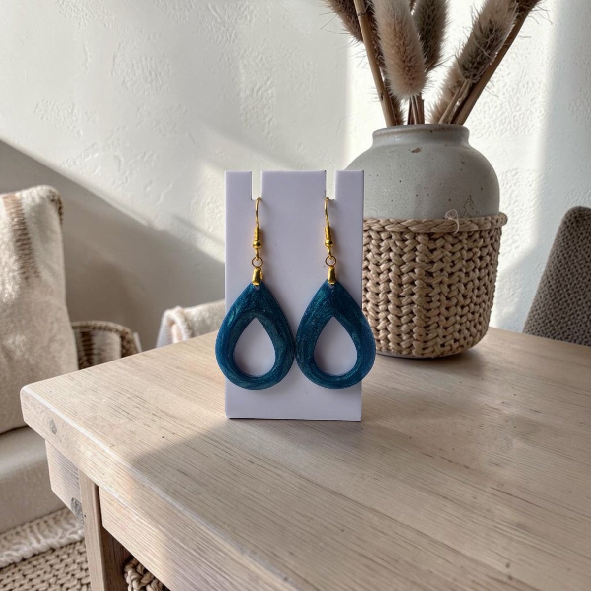 Mirabilia Boutique’s Mermaid Dust Teardrop Earrings with gold hooks are shown on a white card atop a light wooden table, accented by a woven basket and neutral decor in the background.