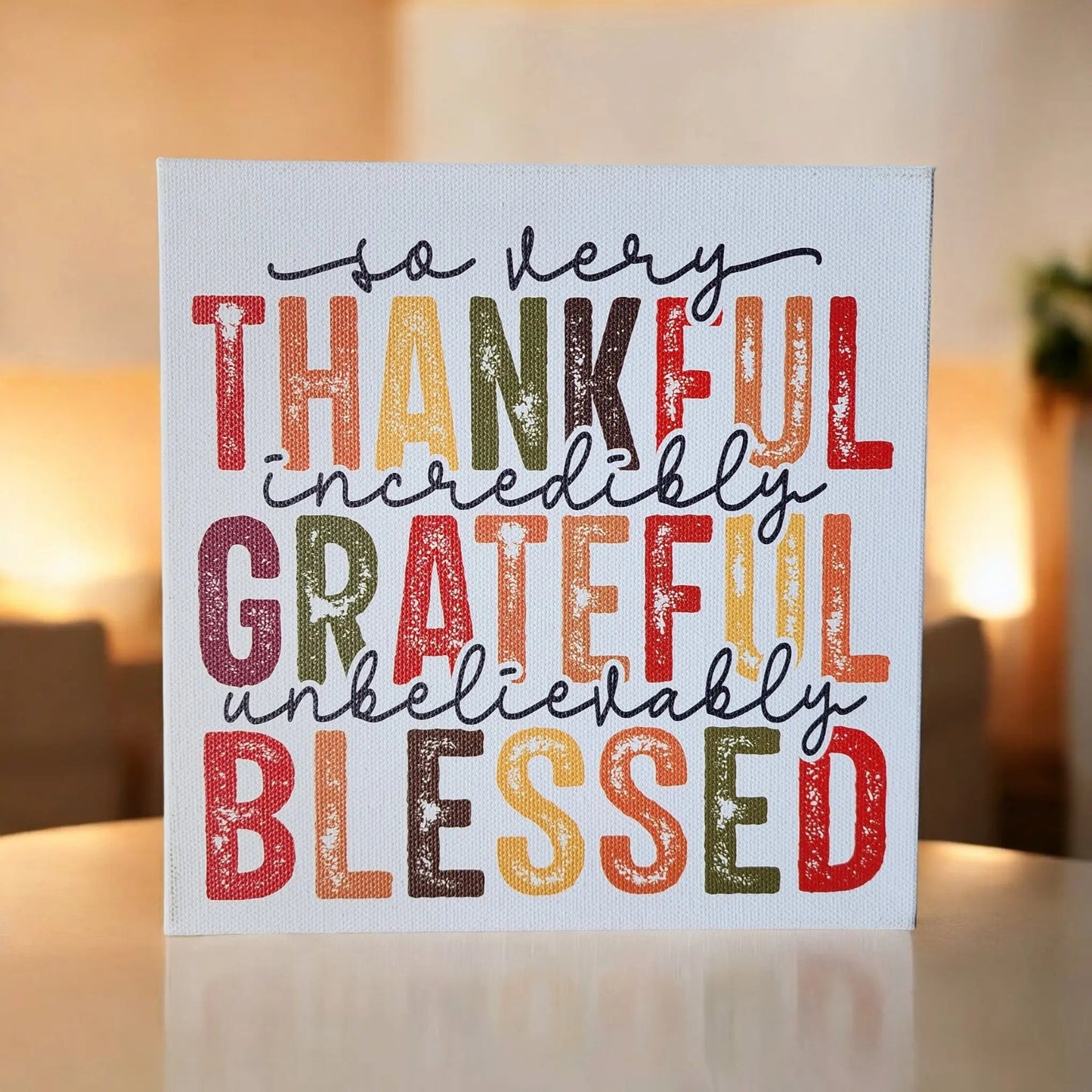 A square canvas from Mirabilia Boutique, titled "Thankful Grateful Blessed Inspirational Sign for Seasonal Home Decor," displays rustic, multicolored text that reads "So very thankful, incredibly grateful, unbelievably blessed." The background is artistically blurred, showcasing Thanksgiving colors in warm lighting with neutral tones and a subtle hint of greenery.