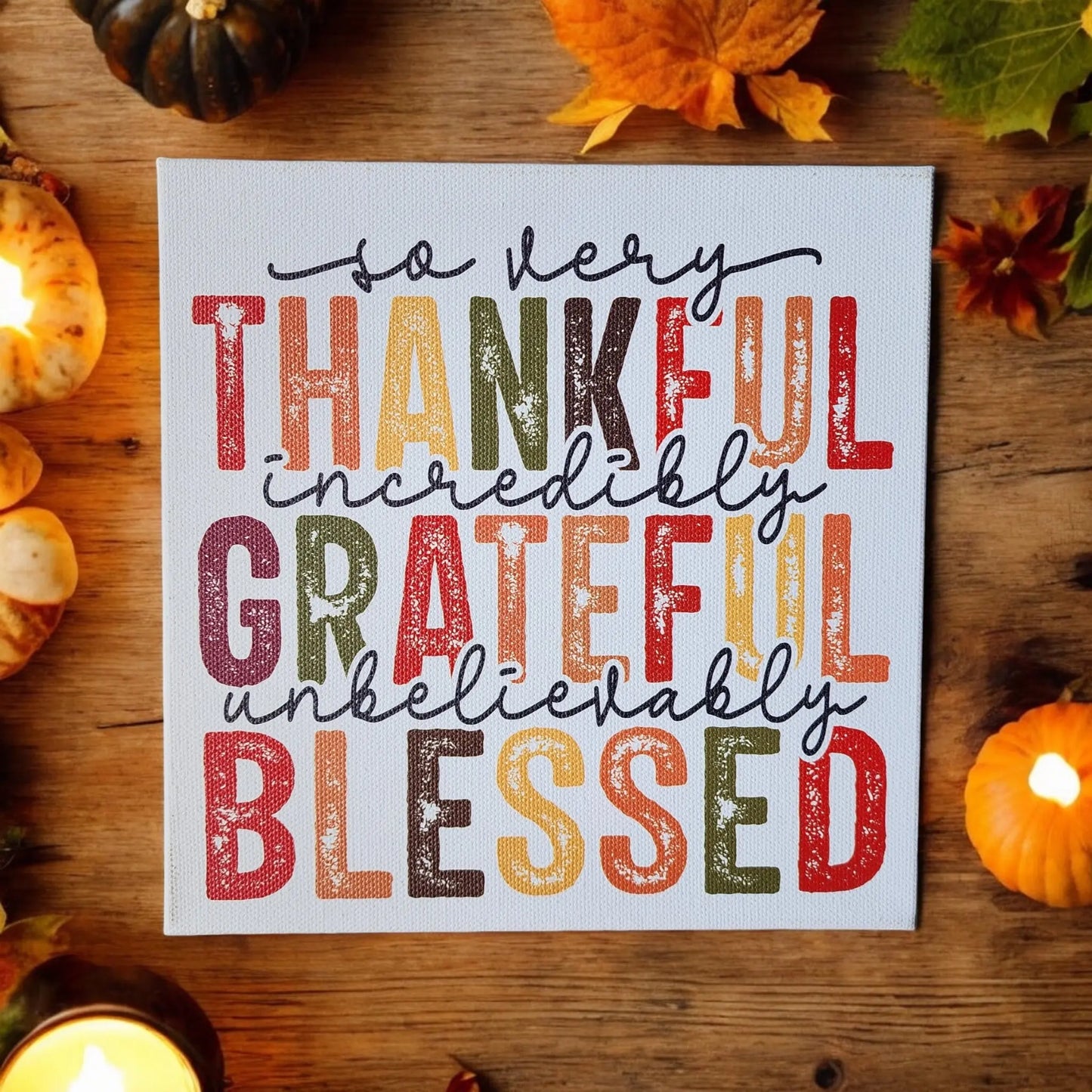 A decorative sign from Mirabilia Boutique's Thankful Grateful Blessed Inspirational Sign collection sits on a wooden surface, surrounded by pumpkins, leaves, and candles. The vibrant Thanksgiving colors of the text read, "So very thankful, incredibly grateful, unbelievably blessed," making it the perfect piece of home decor for the season.