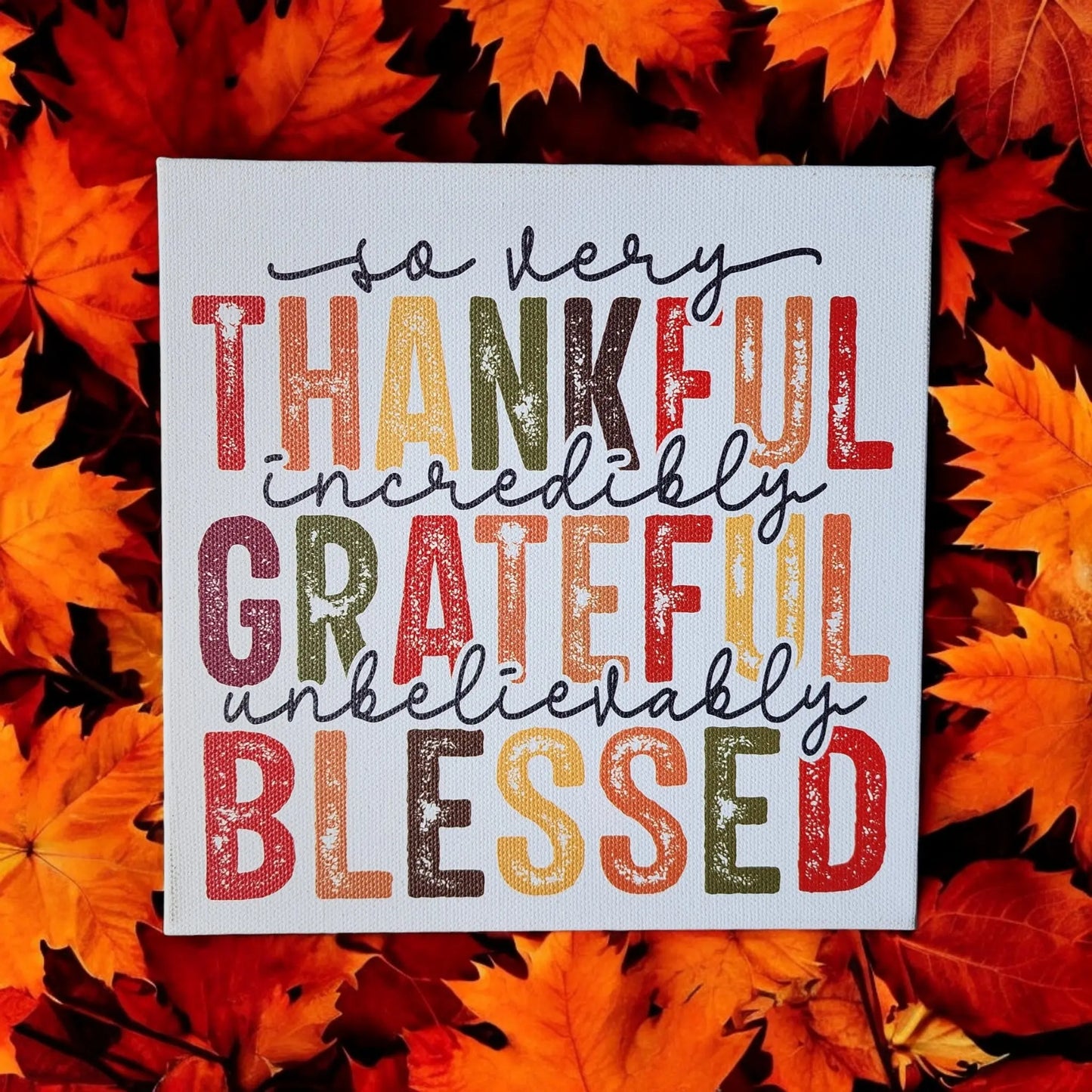 The Mirabilia Boutique's Thankful Grateful Blessed Inspirational Sign for Seasonal Home Decor, featuring the words "so very thankful, incredibly grateful, unbelievably blessed" in vibrant colors and surrounded by orange and red autumn leaves, is the perfect addition to your home for the Thanksgiving season.