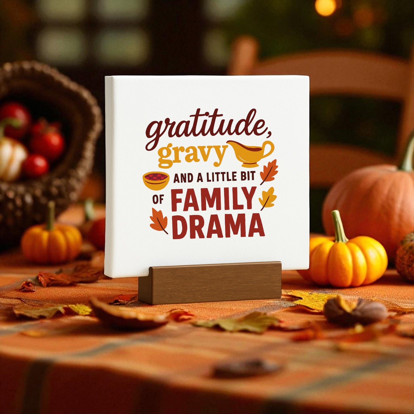 A table with pumpkins, leaves, and fruit sets a cozy Thanksgiving scene, featuring Mirabilia Boutique’s “Gratitude Gravy & Drama” funny mini sign on a stand with festive autumn graphics.