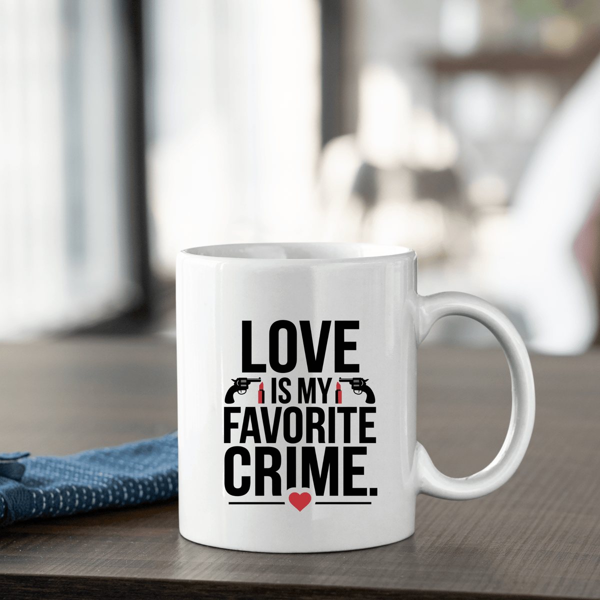 The Love Is My Favorite Crime Mug by Mirabilia Boutique sits on a wooden table with bold lettering, gun and handcuff icons, and a red heart—perfect true crime Valentine gift for podcast fans. A blue napkin is folded beside it.