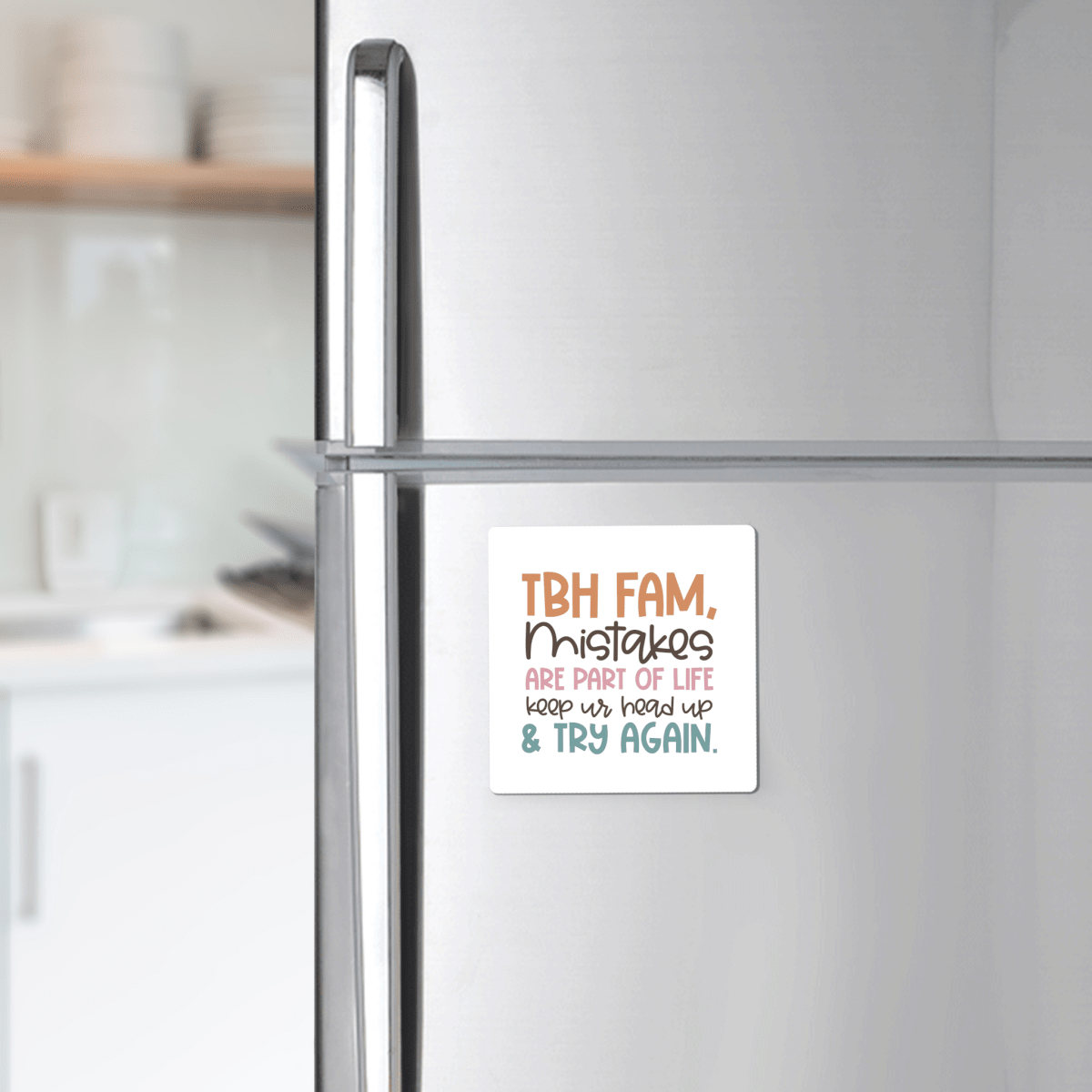 A Mirabilia Boutique Growth Mindset Teacher Magnet with the quote "Try Again" is displayed on a refrigerator. The magnet reads, "TBH FAM, Mistakes are part of life. Keep ur head up & try again." Kitchen shelves and dishes appear in the background.