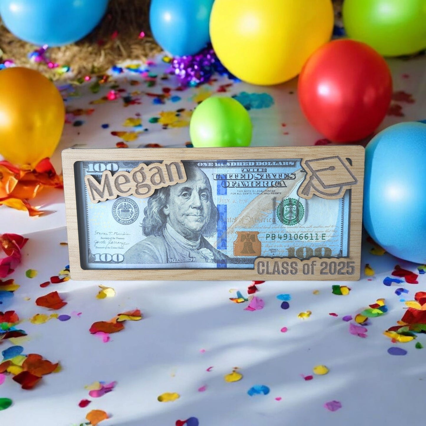 A Personalized Graduation Money Holder by Mirabilia Boutique, custom engraved with “Megan” and “Class of 2025,” displayed amid balloons and confetti as a unique graduation gift.